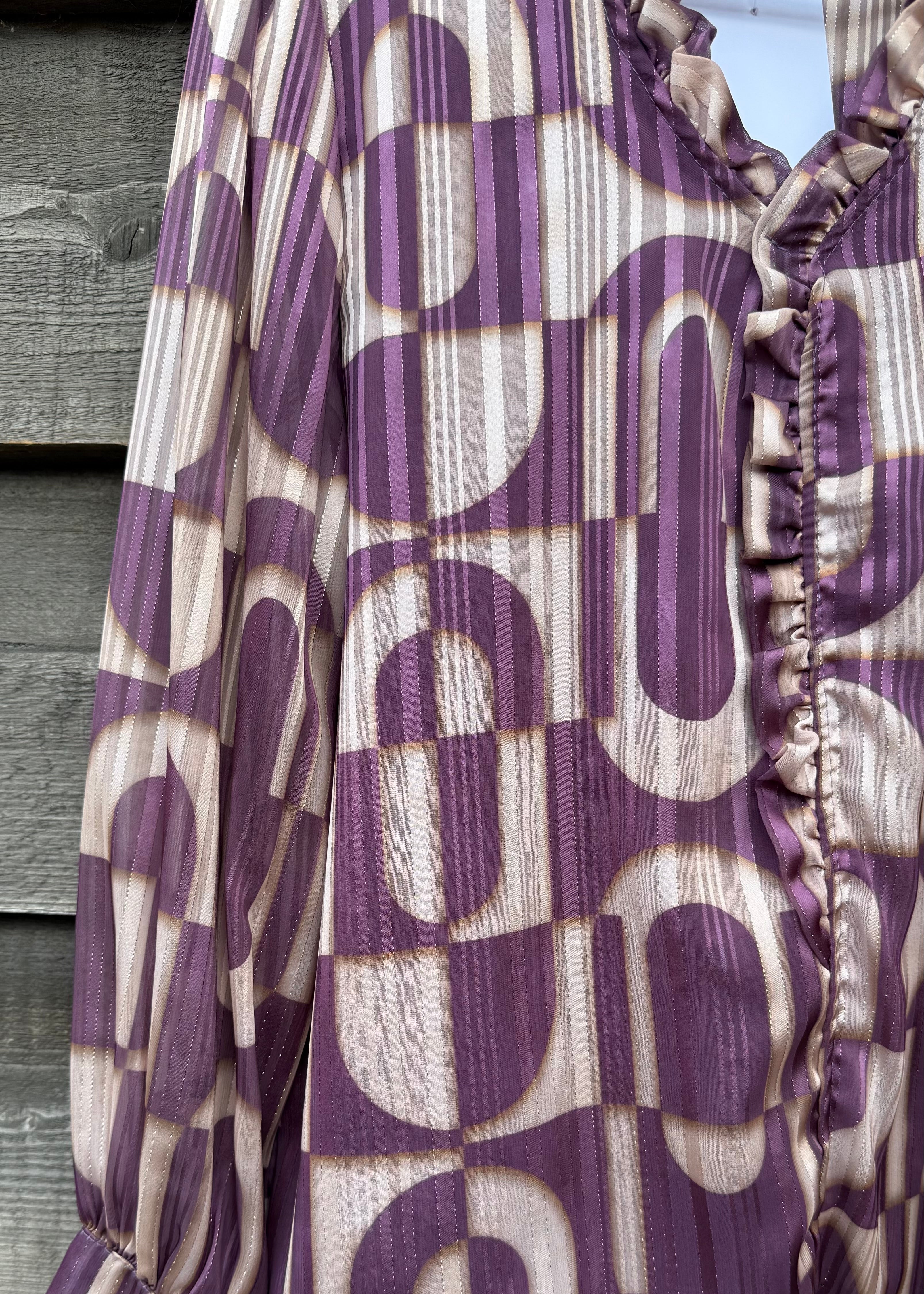 Purple and beige patterned blouse with ruffled details on a wooden surface.