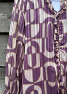 Purple and beige patterned blouse with ruffled details on a wooden surface.