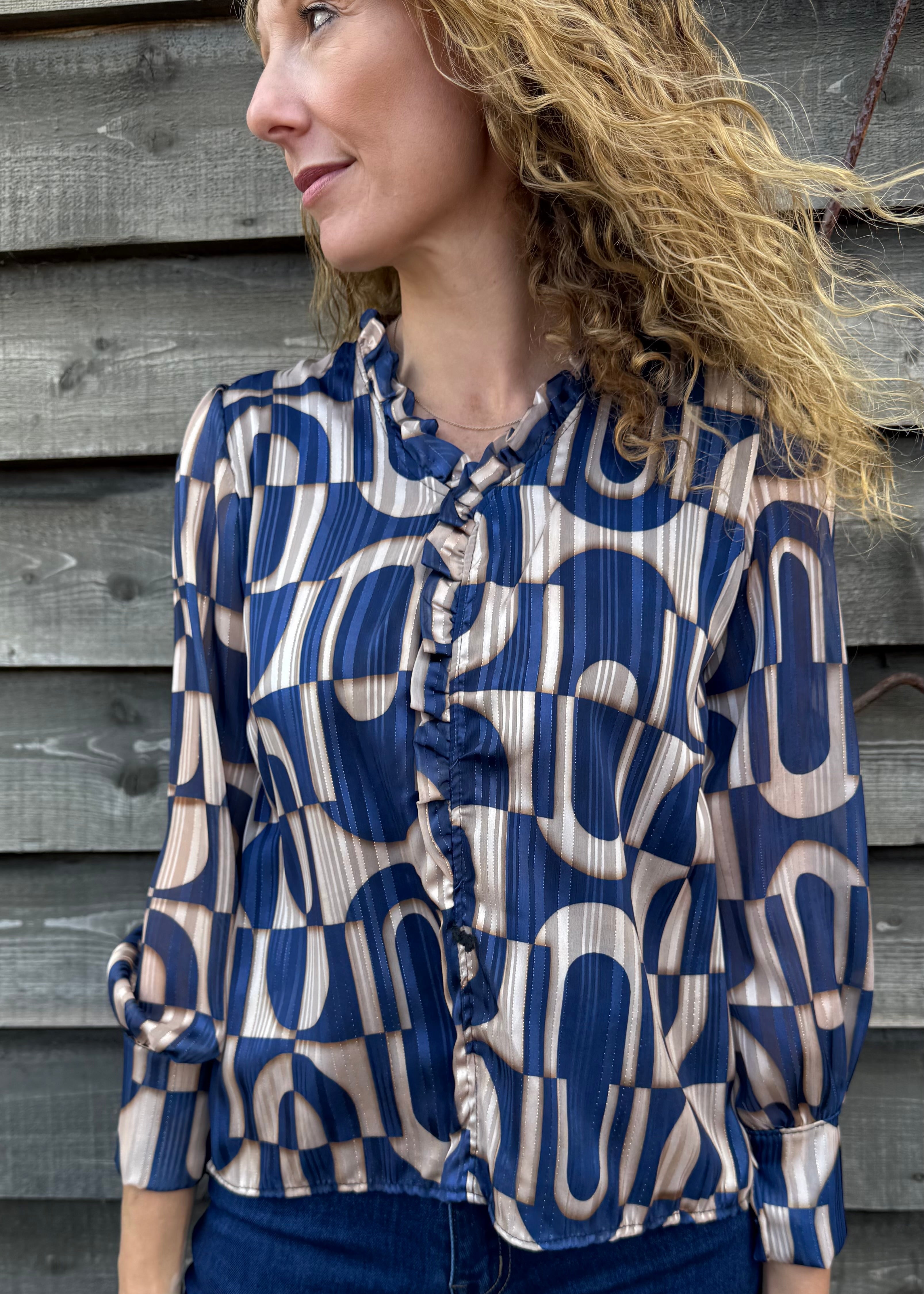 Woman wearing a blue and beige patterned blouse against a wooden wall.
