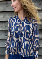 Woman wearing a blue and beige patterned blouse against a wooden wall.