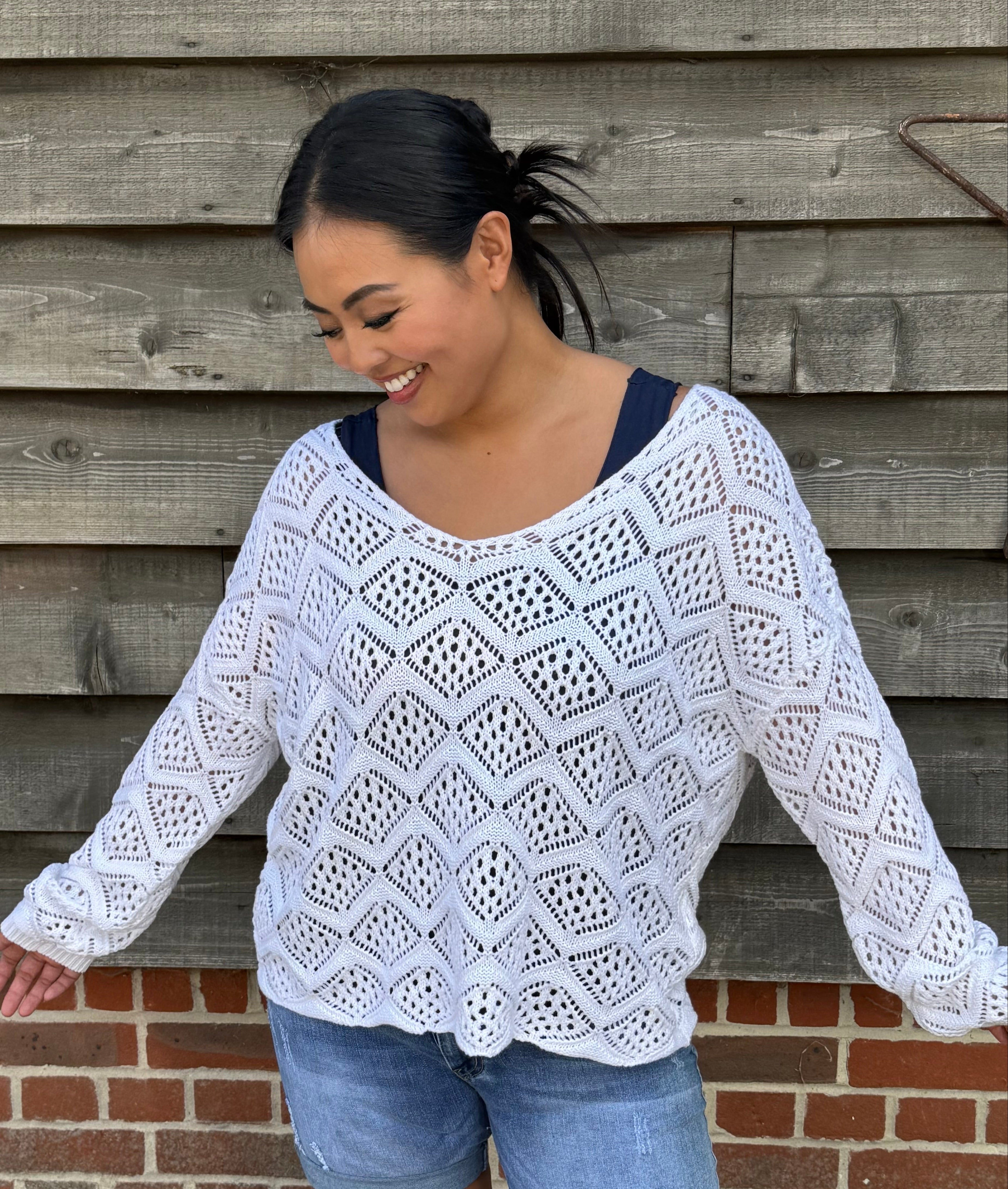 Woman wearing a white crochet top and denim shorts standing against a wooden wall.