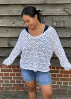 Woman wearing a white crochet top and denim shorts standing against a wooden wall.