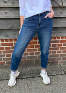 Person wearing blue jeans and white sneakers standing against a brick wall.