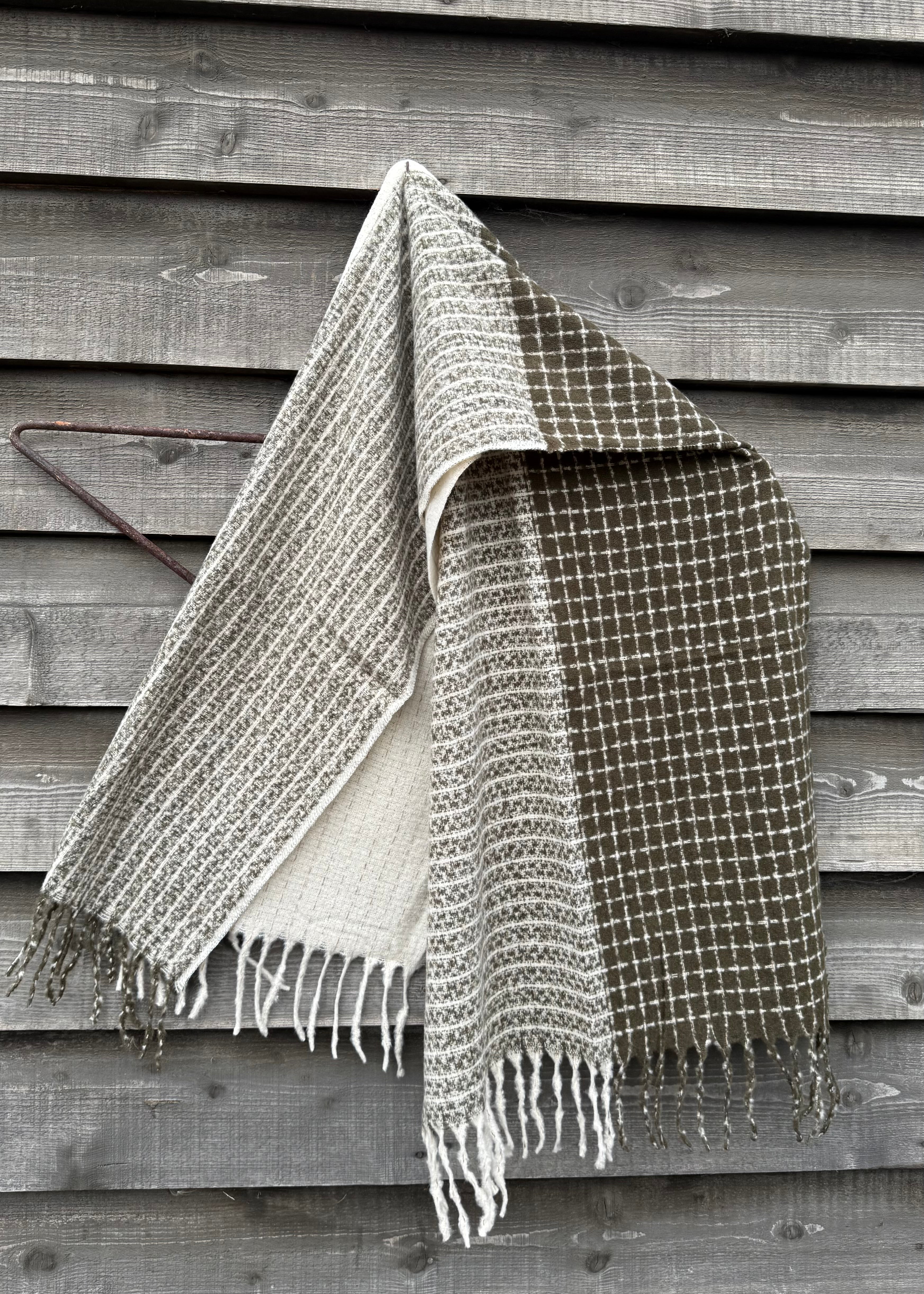 Woven blanket with fringes draped over a wooden surface