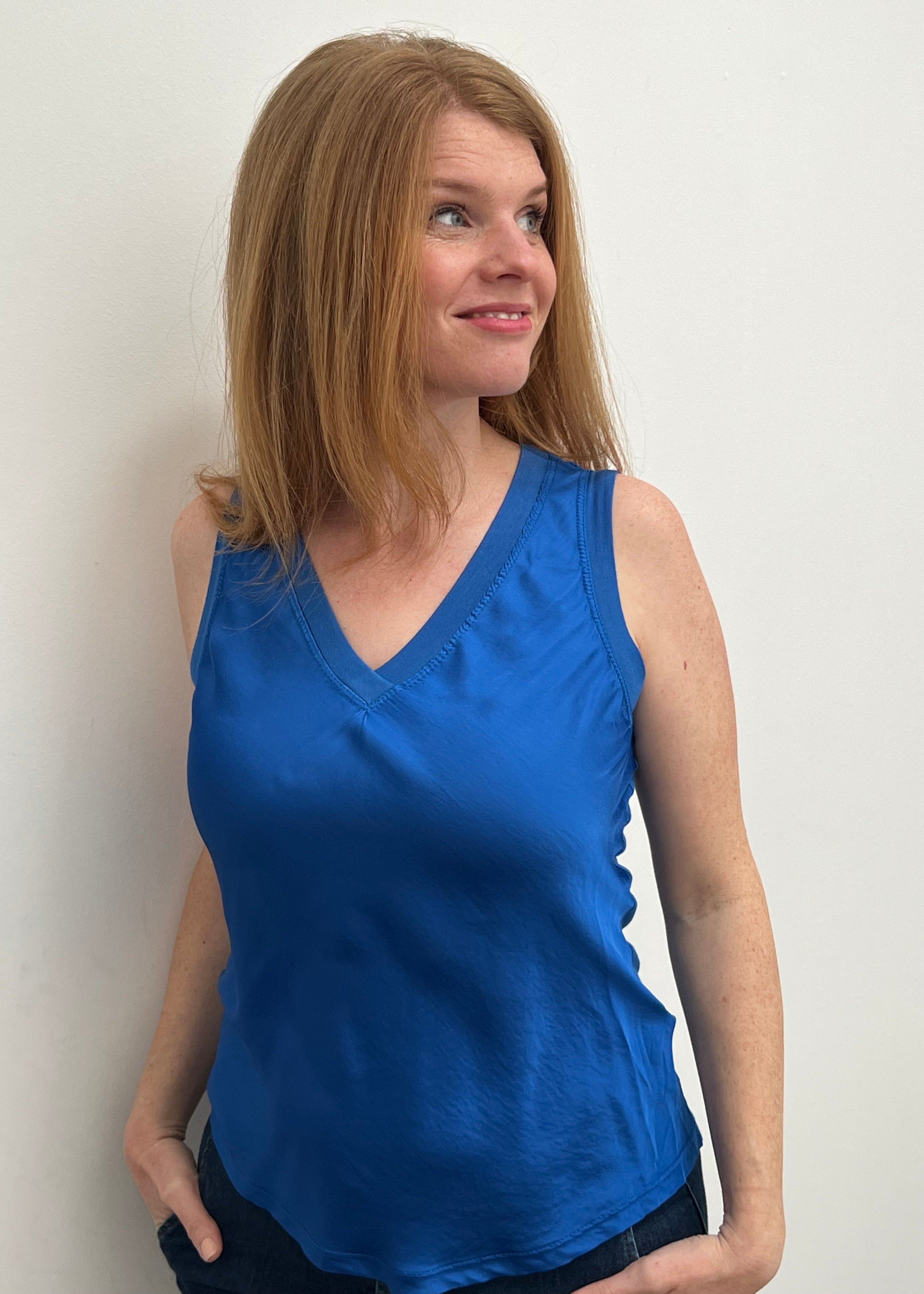 A woman smiling and wearing a blue sleeveless top with a V-neckline, made of silk and viscose fabric.
