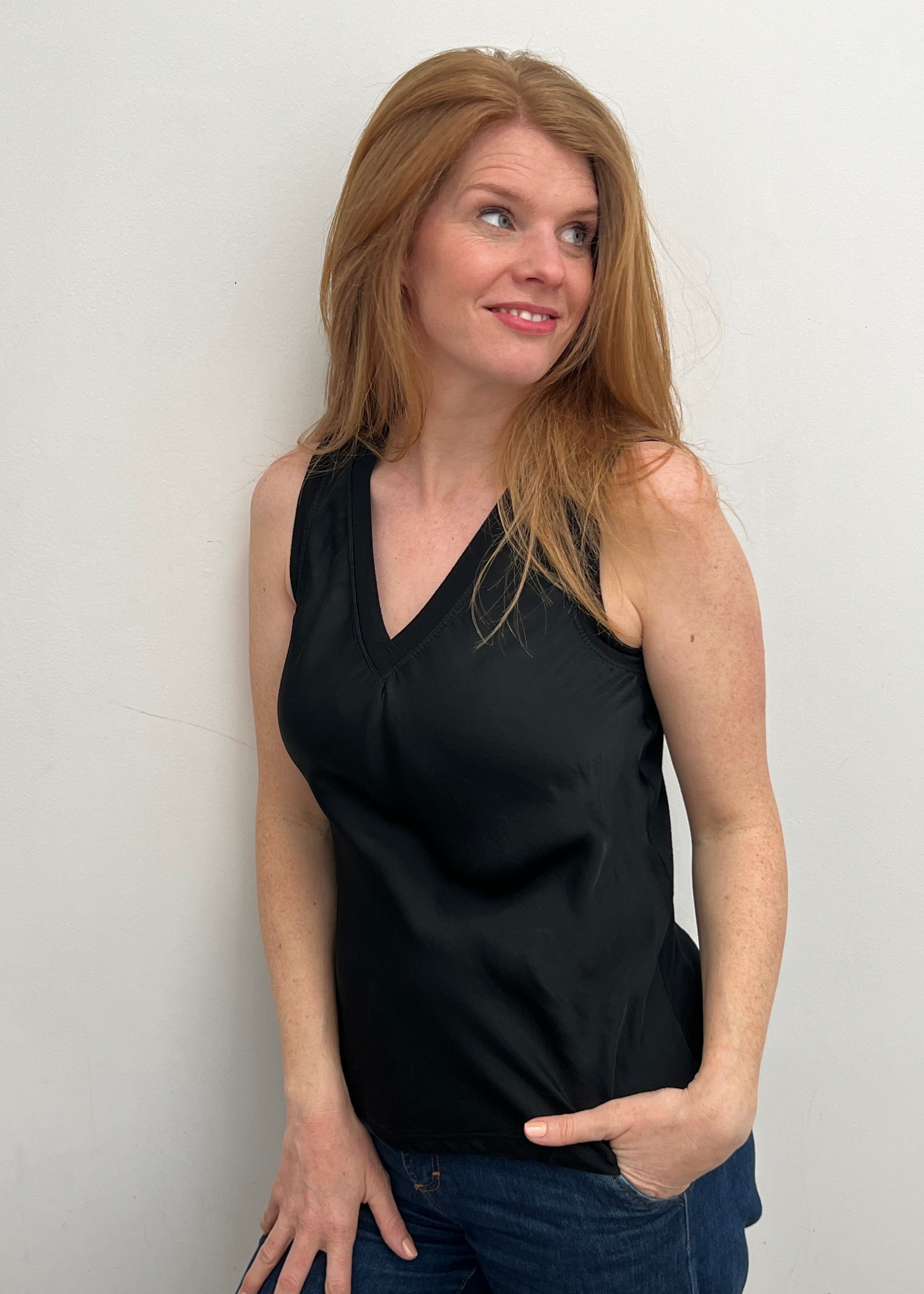 A woman smiling and wearing a black sleeveless top with a V-neckline, made of silk and viscose fabric.