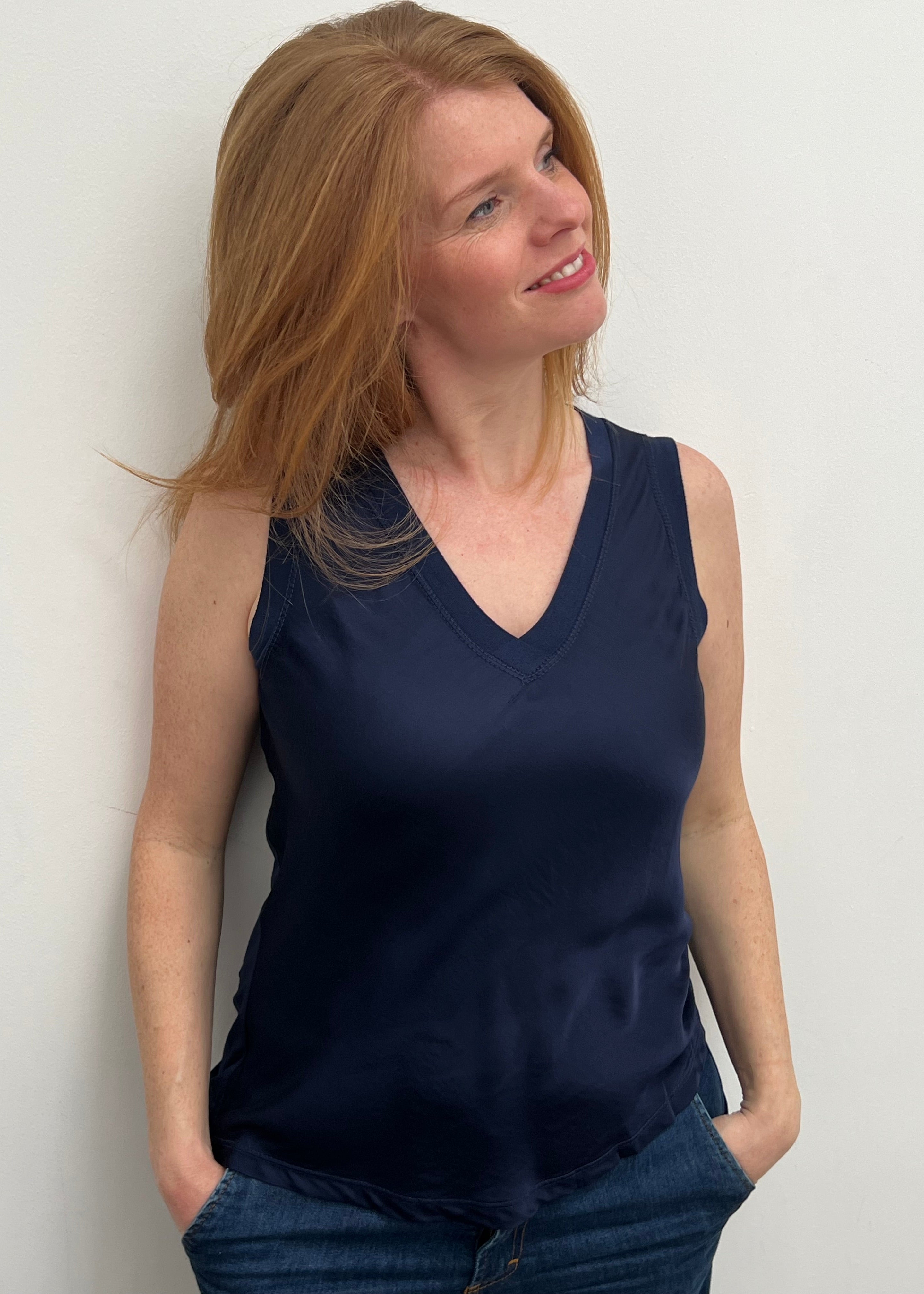 A woman smiling and wearing a blue sleeveless top with a V-neckline, made of silk and viscose fabric.