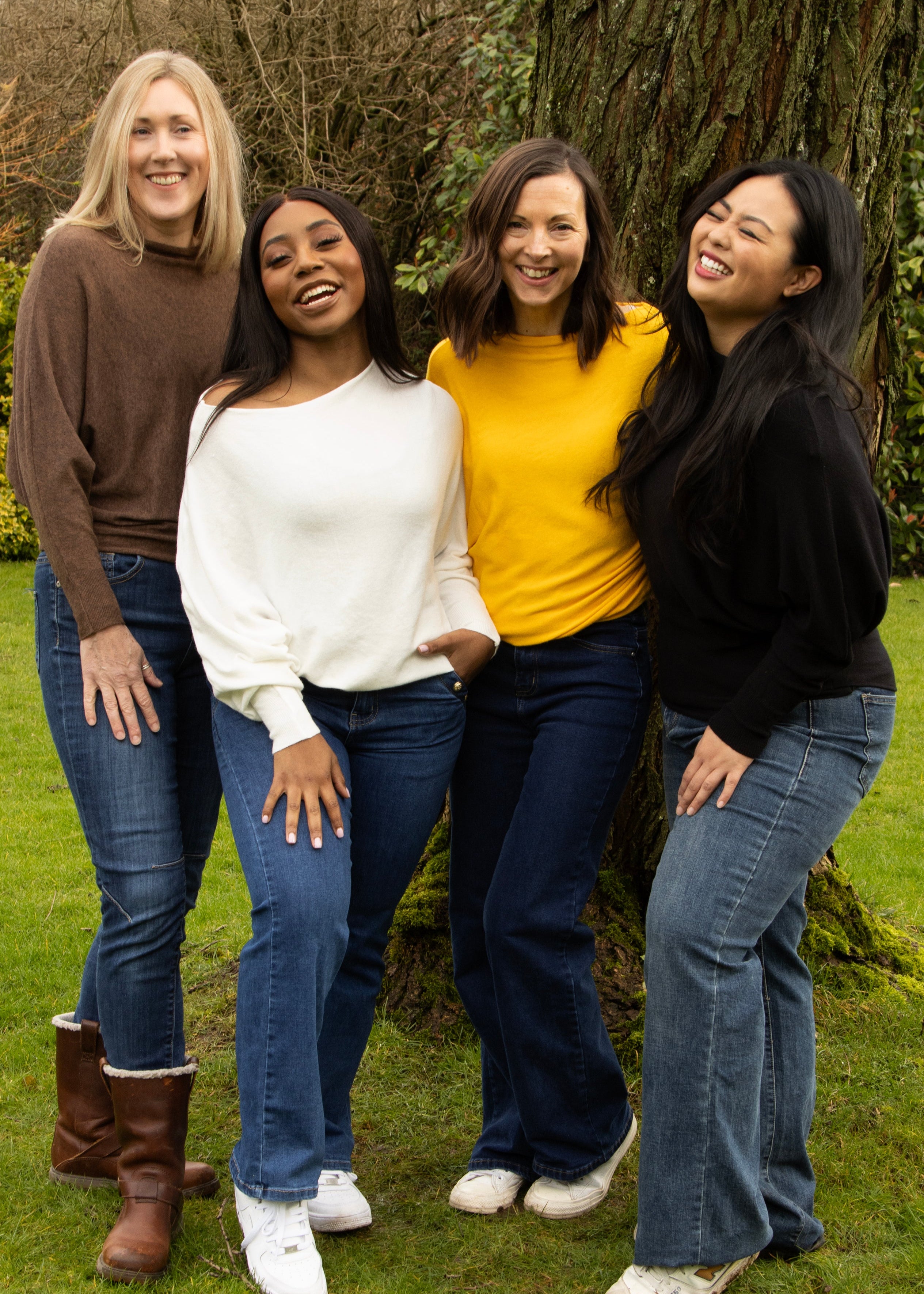 Four women standing outdoors wearing different colored jumpers. From left to right: brown, white, yellow, and black.