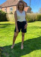 A person wearing black shorts and a beige tank top, standing on grass with a house and trees in the background.