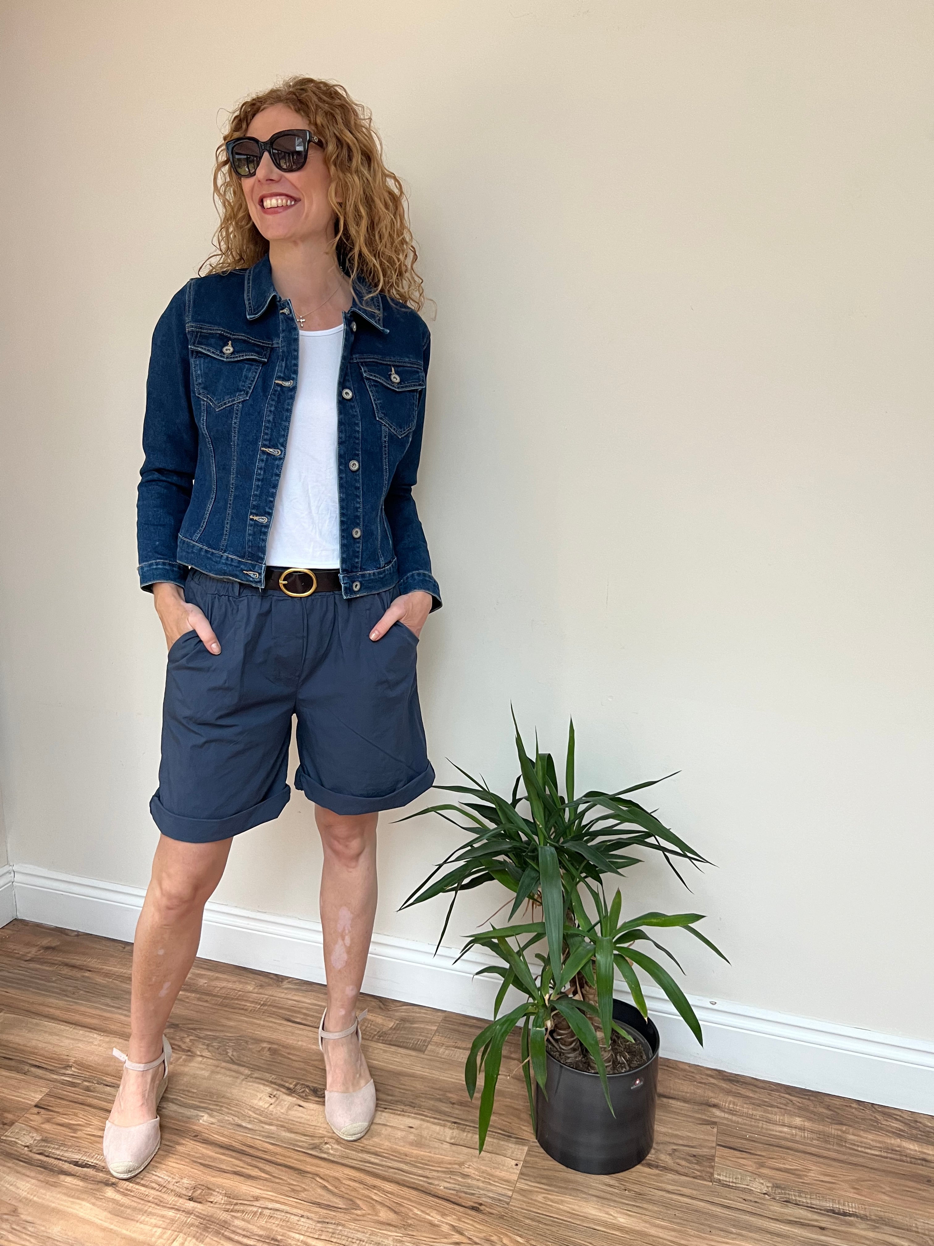 A person wearing black shorts and a beige tank top, standing on grass with a house and trees in the background.