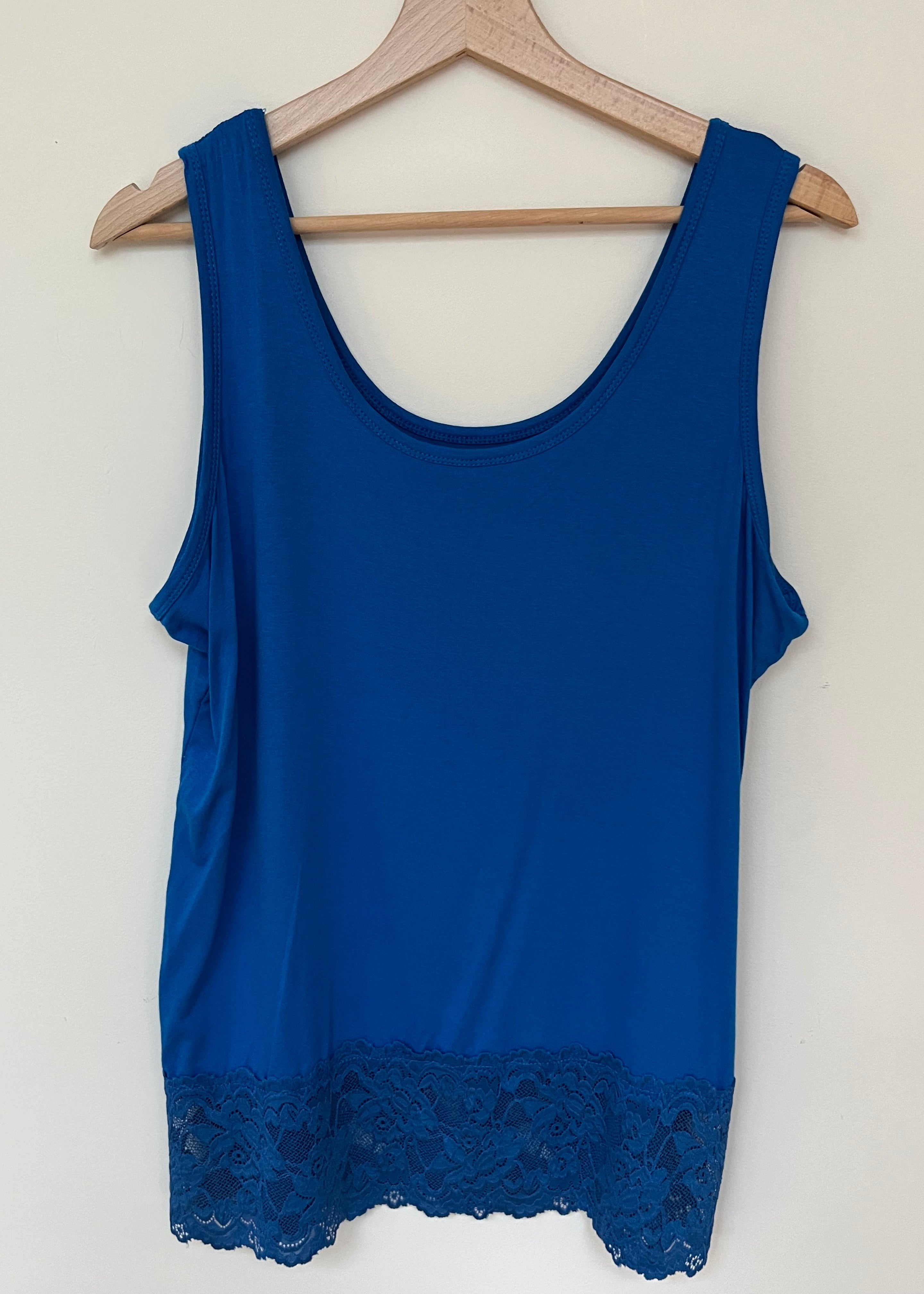 A woman wearing a pink sleeveless vest with a lace hem, paired with blue jeans.