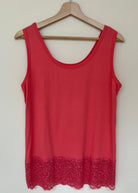 A woman wearing a pink sleeveless vest with a lace hem, paired with blue jeans.