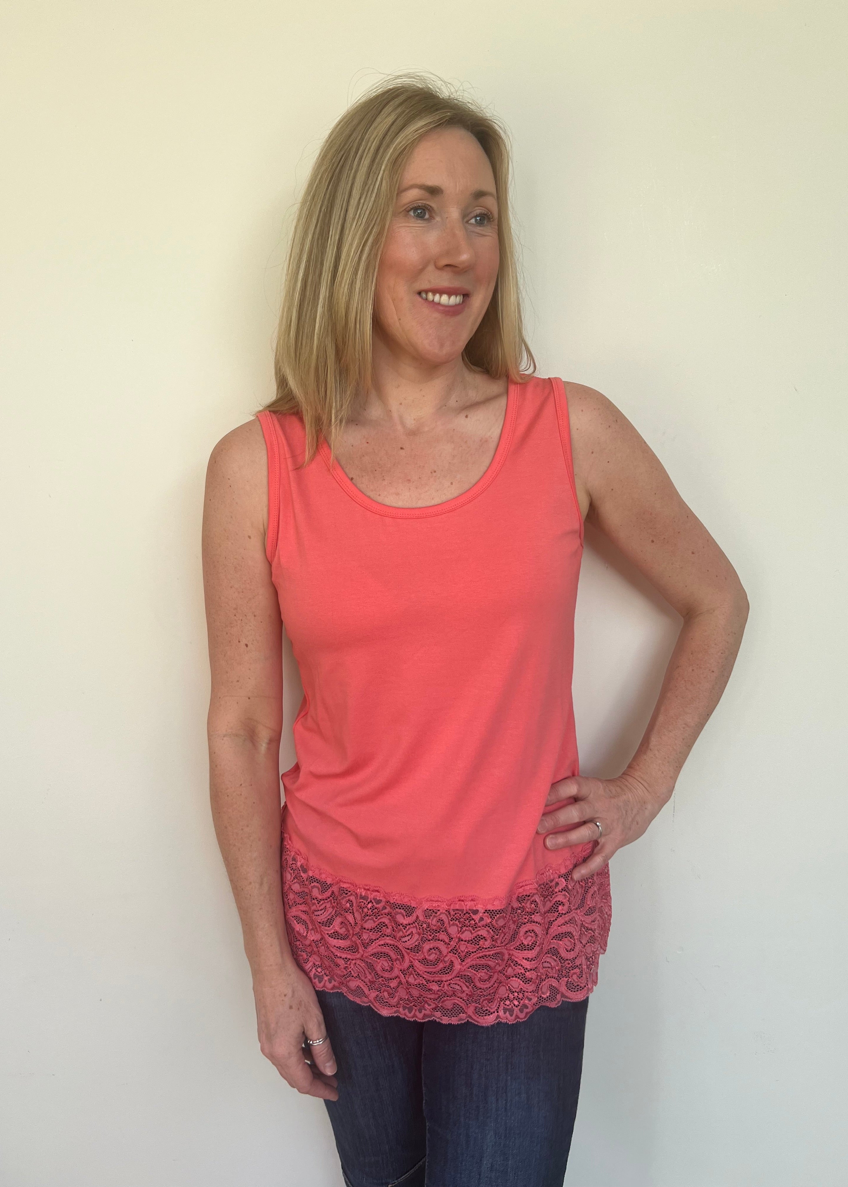 A woman wearing a pink sleeveless vest with a lace hem, paired with blue jeans.