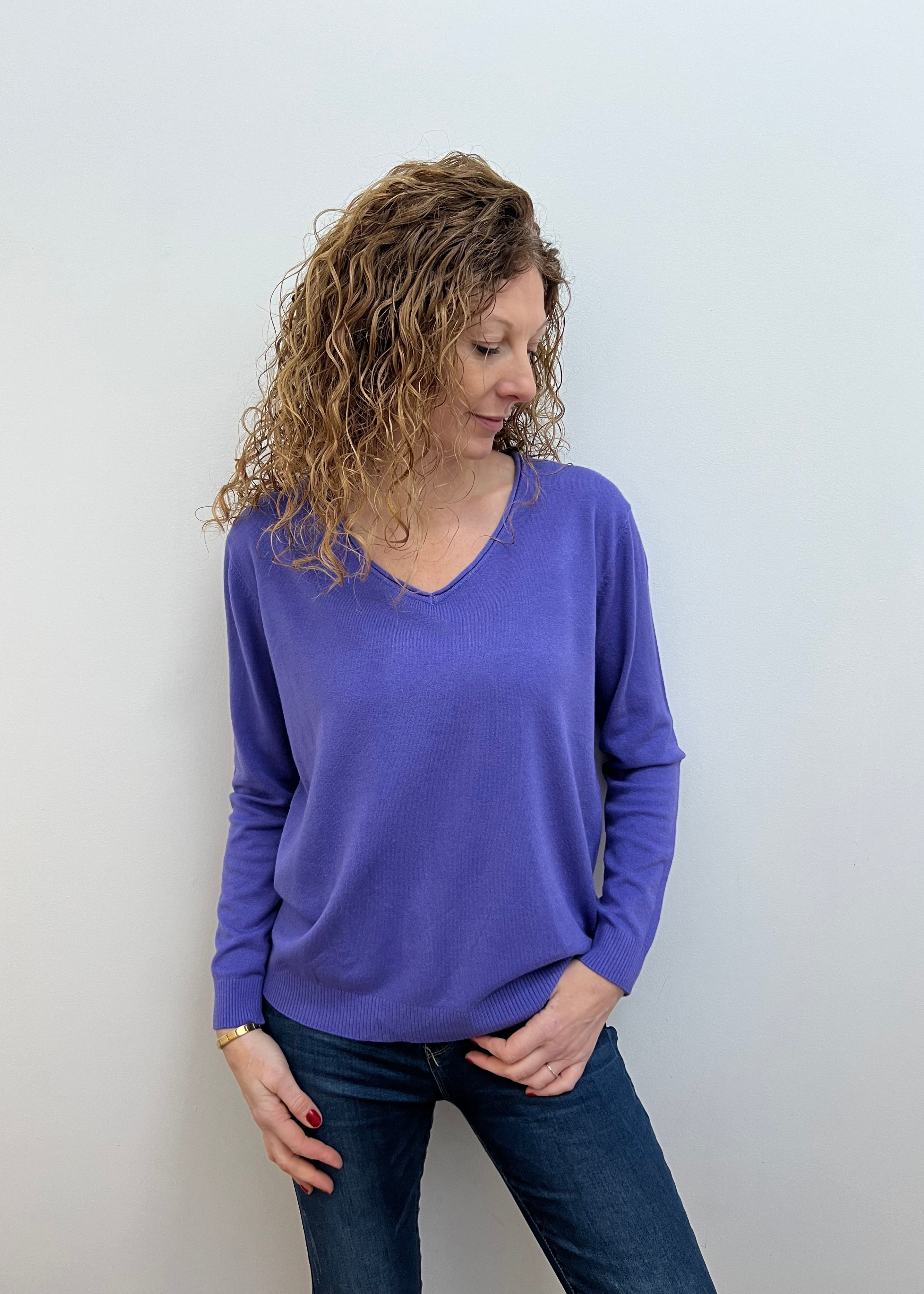 A woman wearing a purple V-neck jumper and blue jeans.