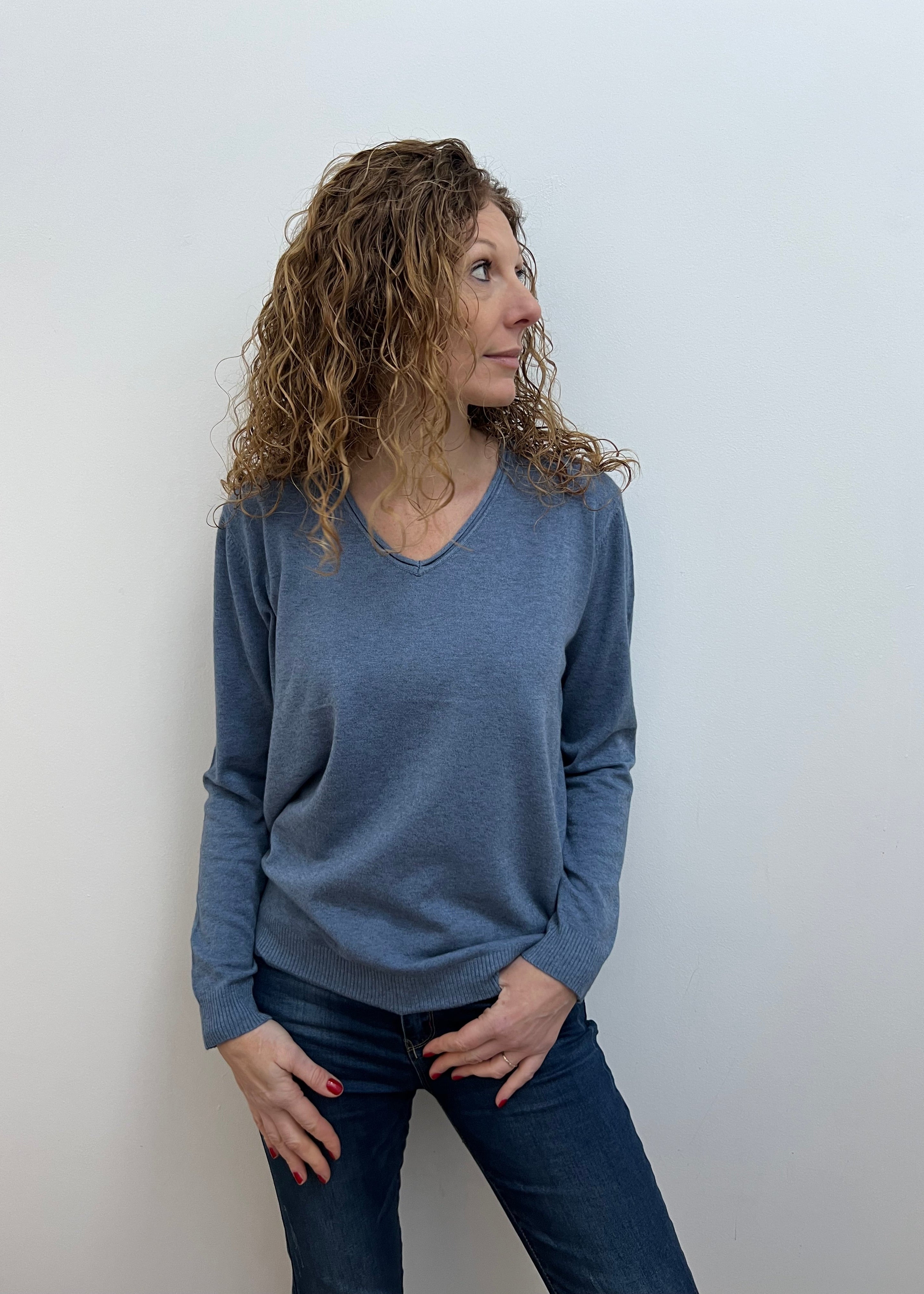 A woman wearing a gray V-neck jumper and blue jeans.