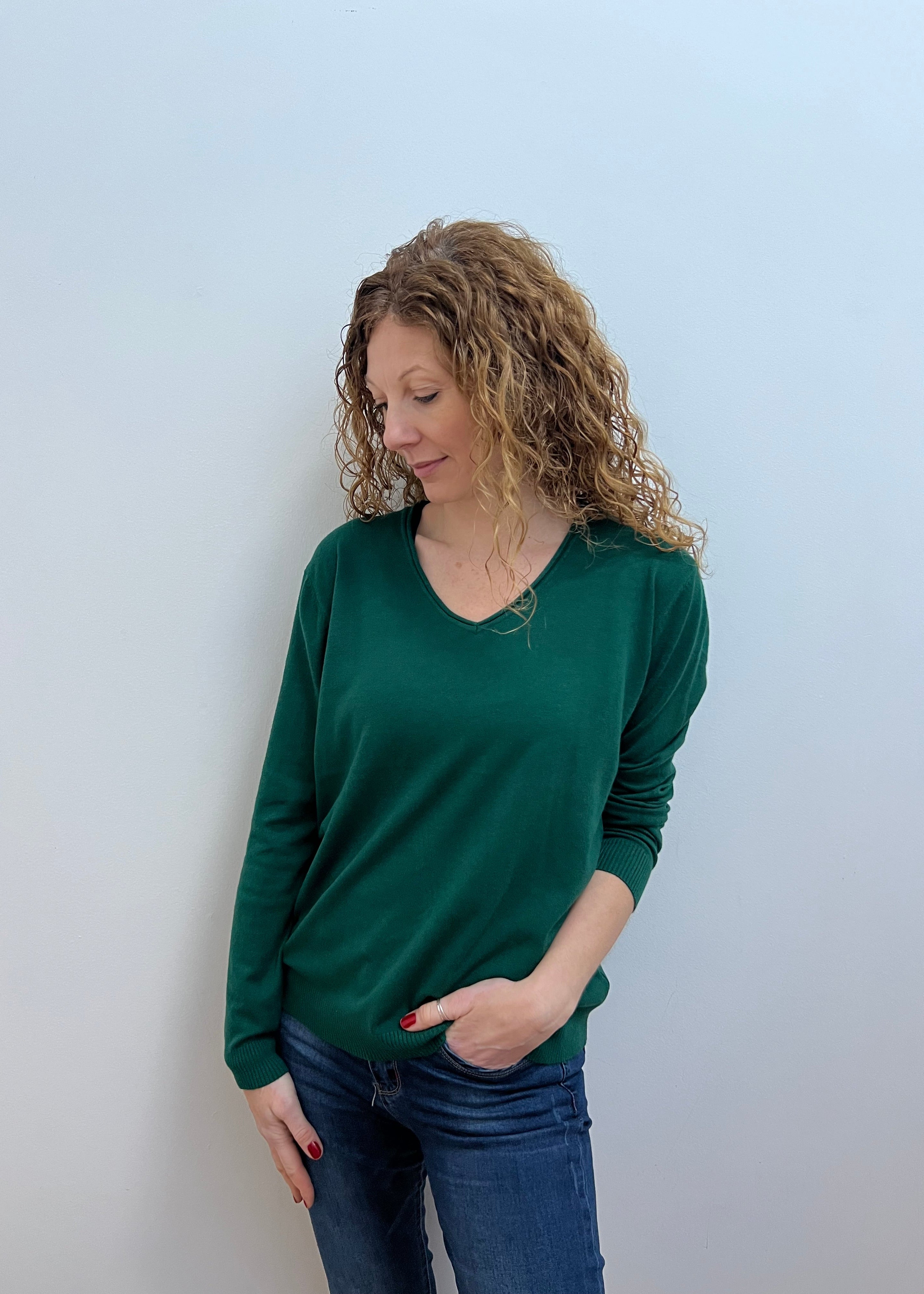 A woman wearing a green V-neck jumper and blue jeans.