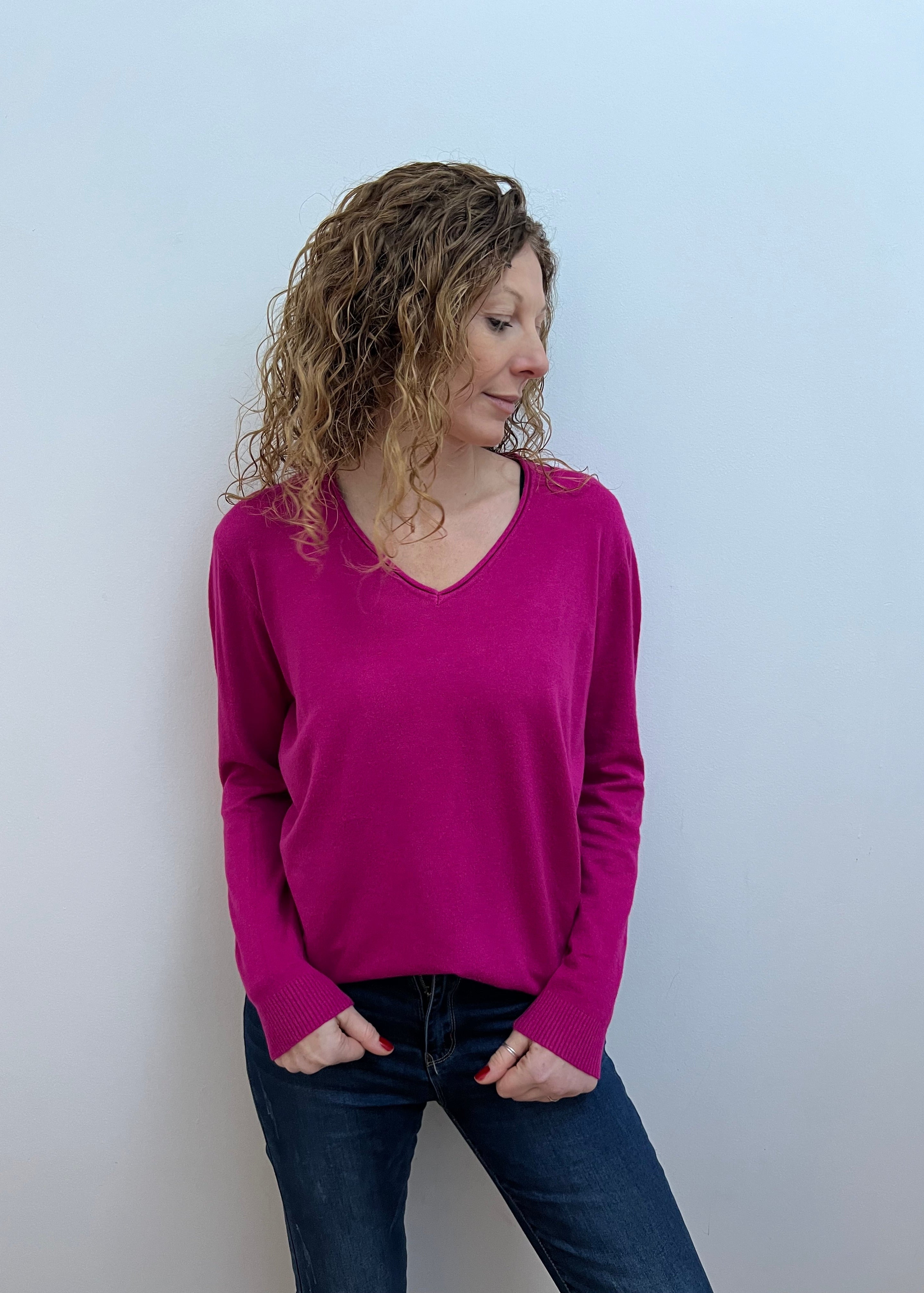 A woman wearing a pink V-neck jumper and blue jeans.