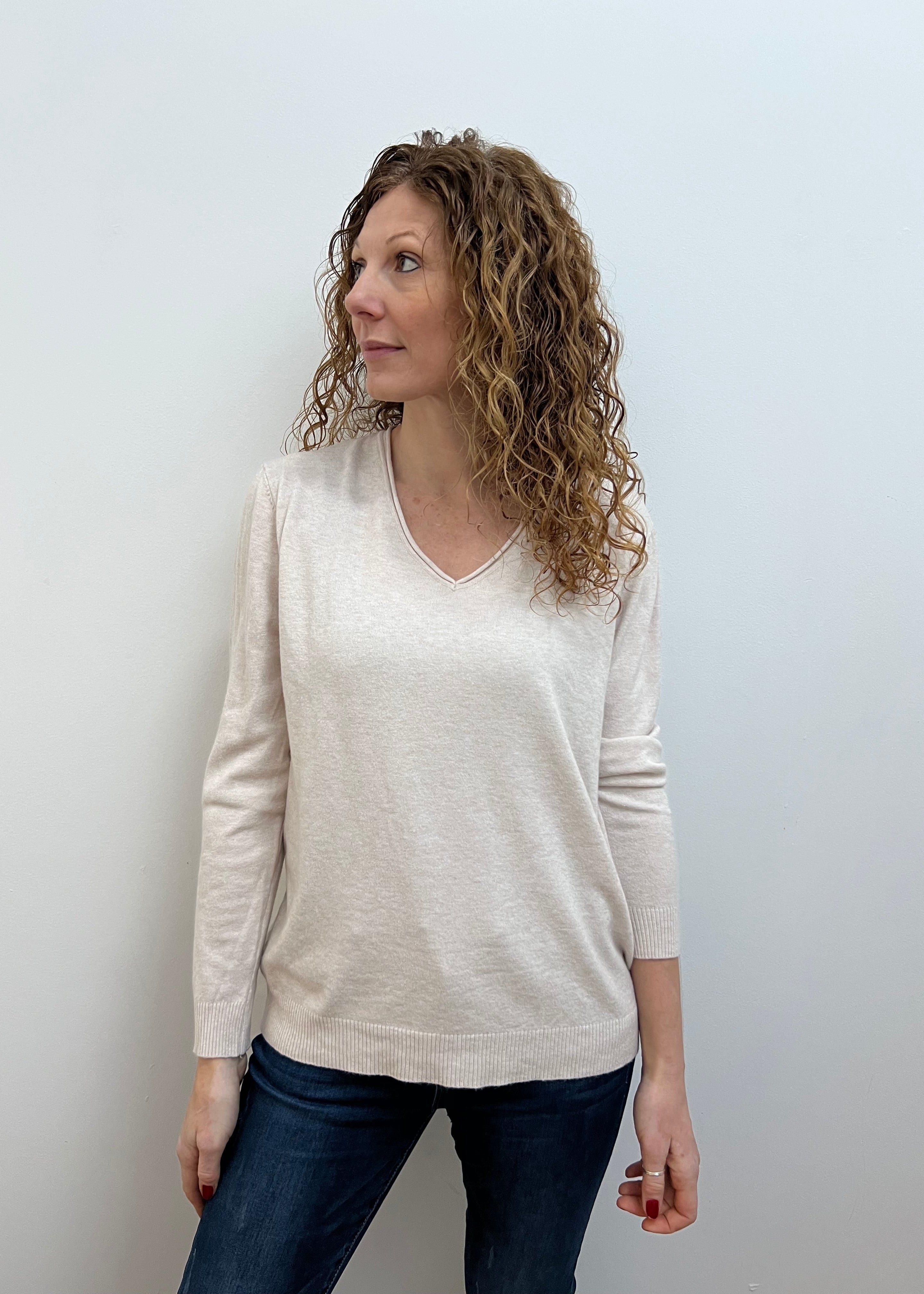 A woman wearing a white V-neck jumper and blue jeans.