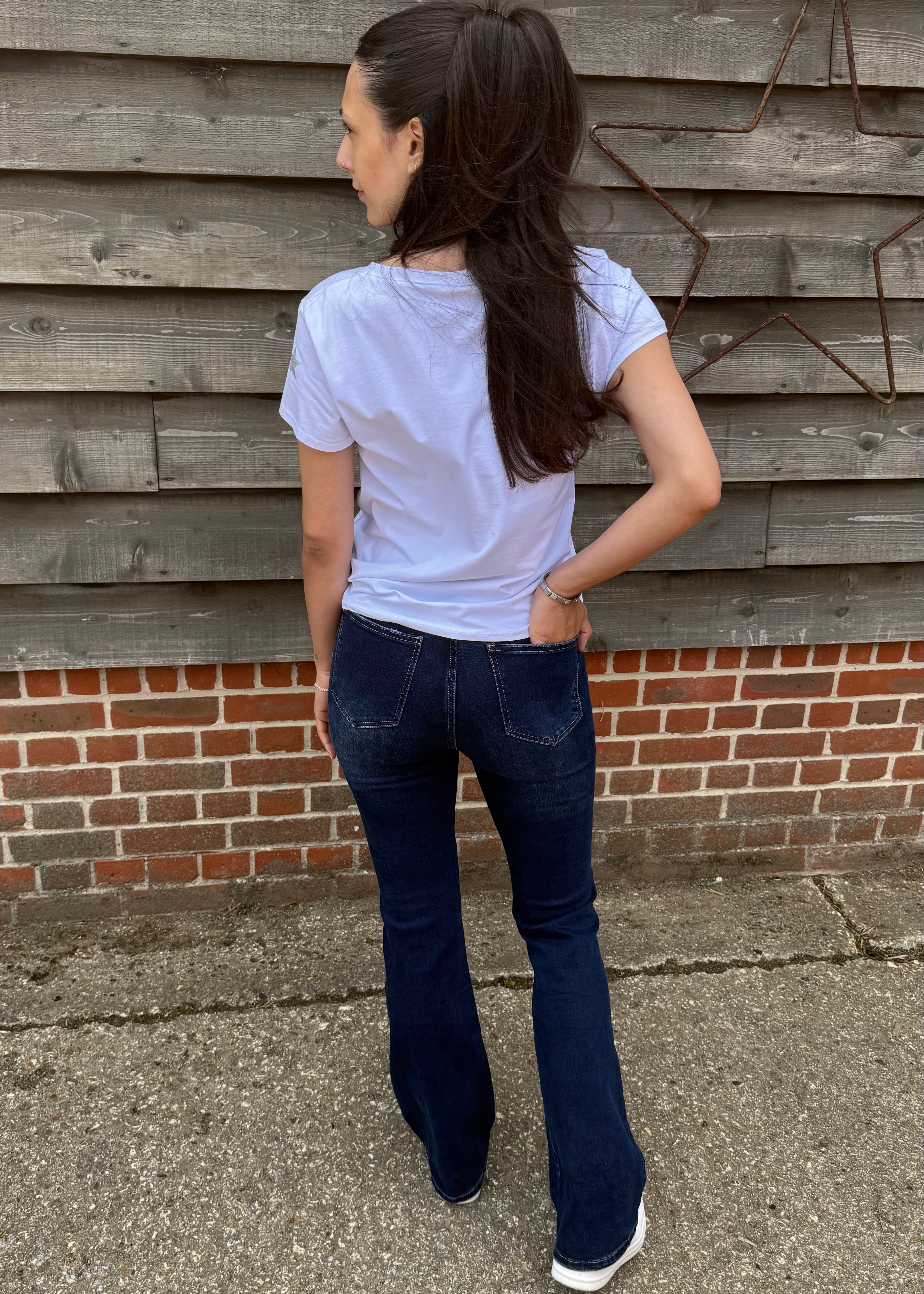 Woman wearing a light blue t-shirt and dark blue jeans standing against a wooden wall.