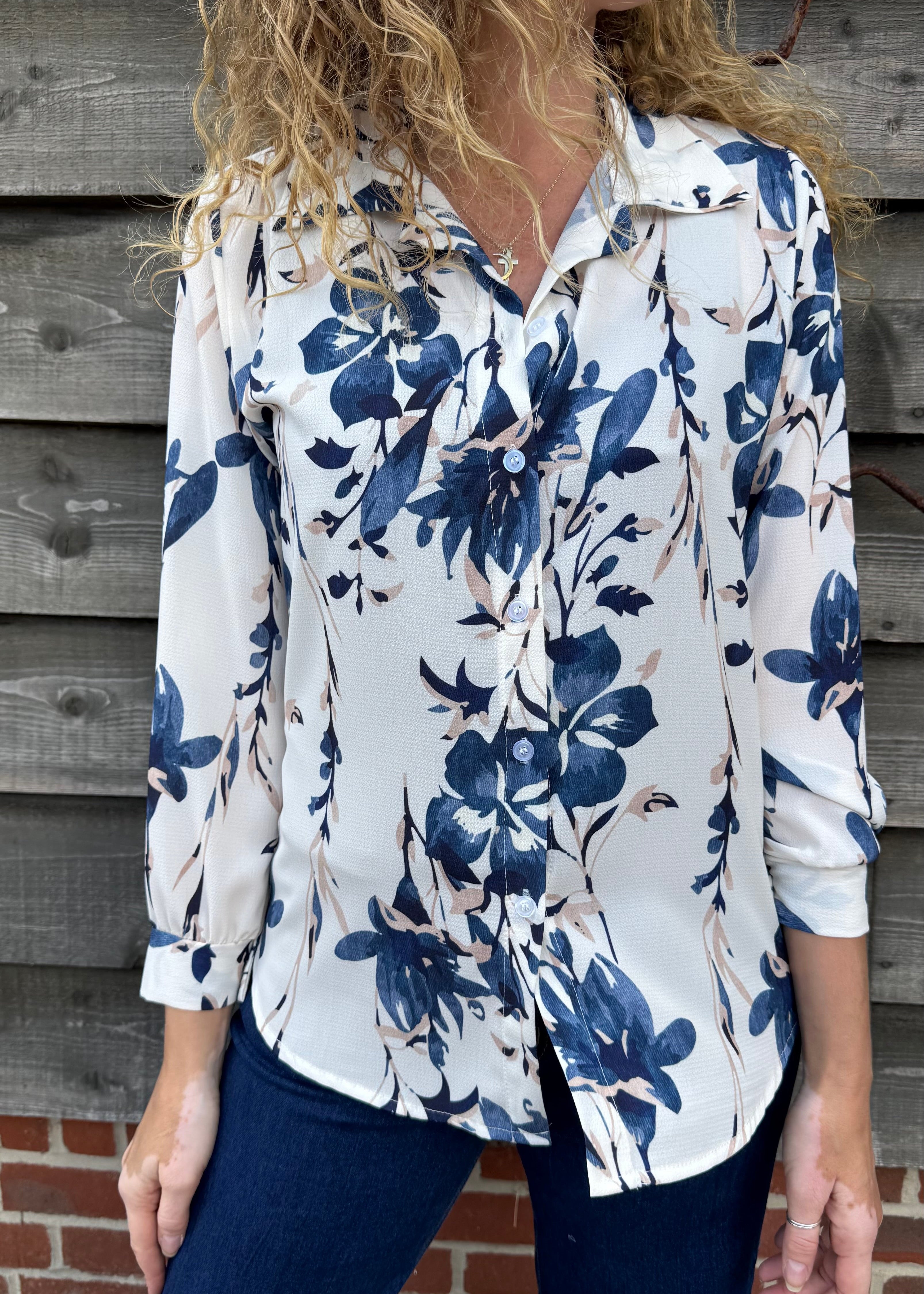 Woman wearing a white blouse with blue floral pattern against a wooden wall.