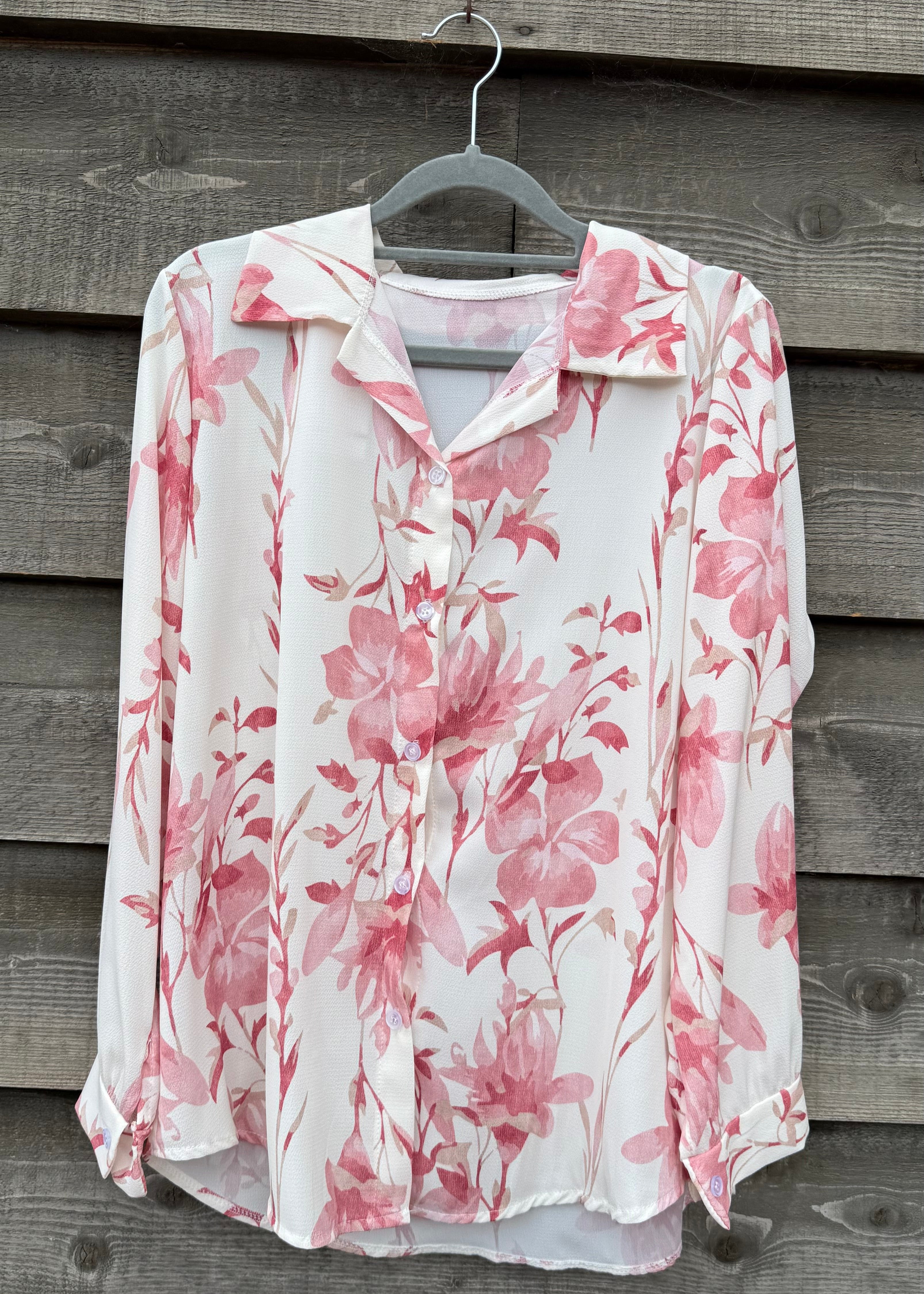 Floral blouse with pink flowers on a hanger against a wooden wall