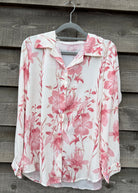 Floral blouse with pink flowers on a hanger against a wooden wall