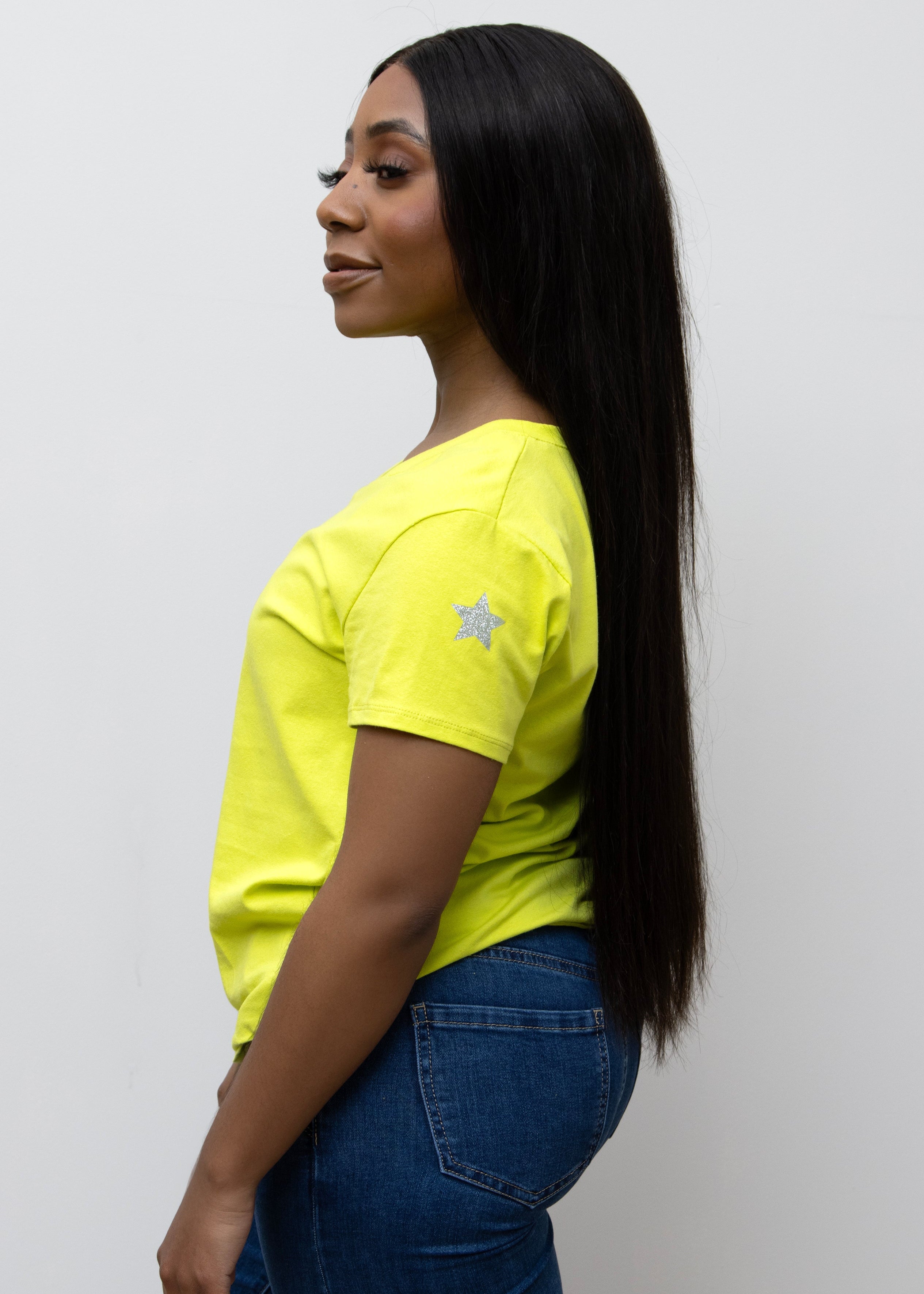 A woman smiling, wearing a pink V-neck T-shirt with a silver star on the sleeve, paired with blue jeans.