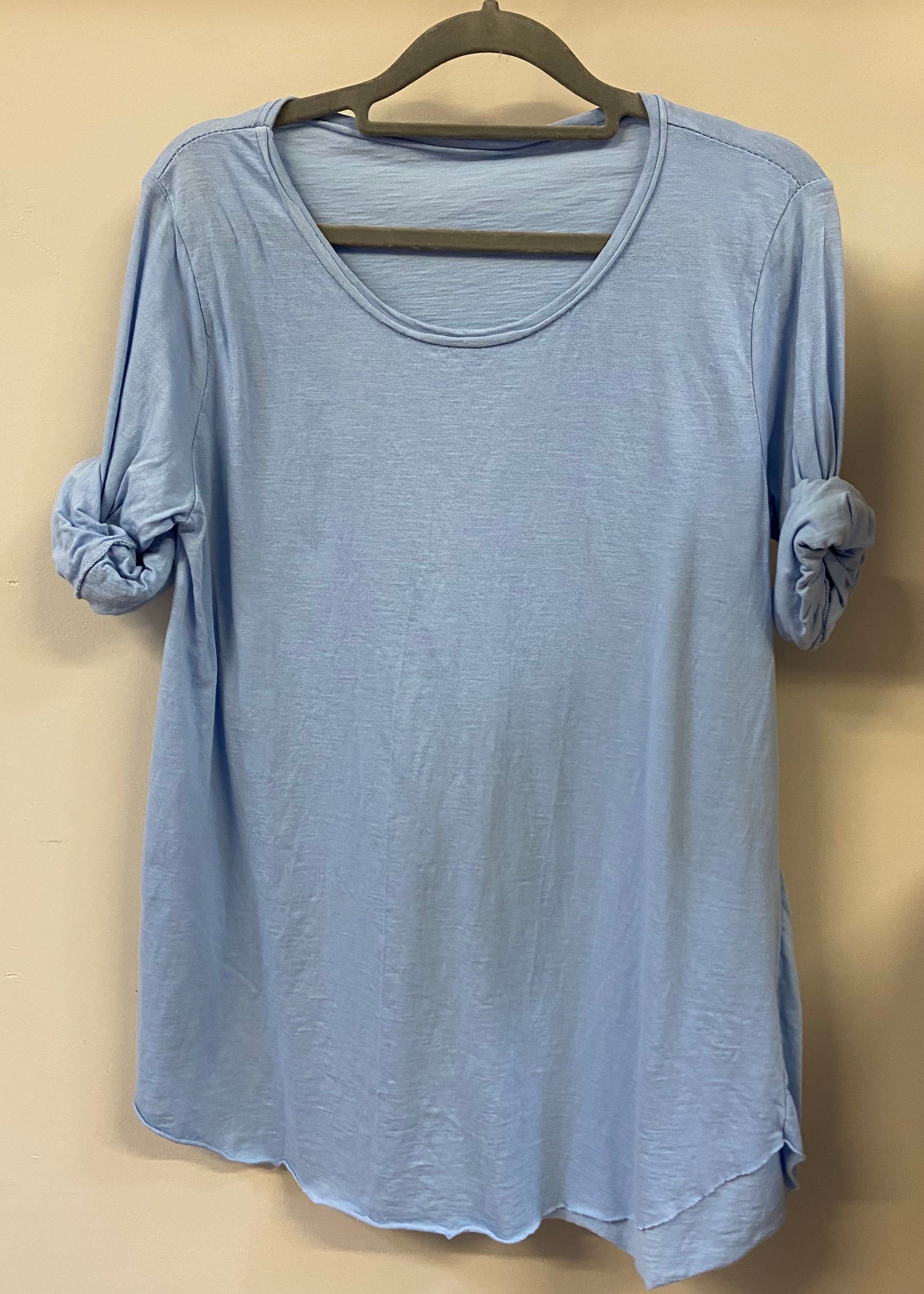 A woman wearing a light blue, long-sleeved cotton top with curved raw edges, in a loose fit style.