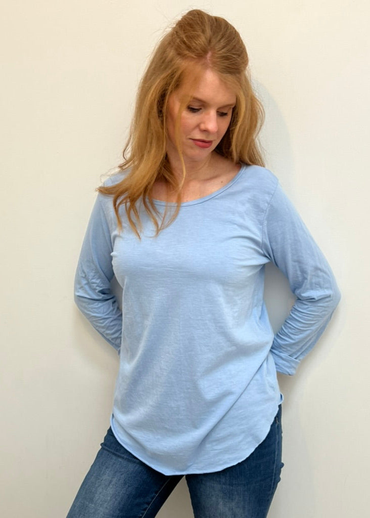A woman wearing a light blue, long-sleeved cotton top with curved raw edges, in a loose fit style.