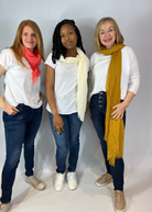 Three people standing next to each other wearing scarves in different colors - red, beige, and yellow.