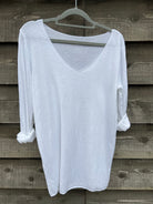 A white, long-sleeved sparkly top hanging on a wooden hanger against a wooden background.
