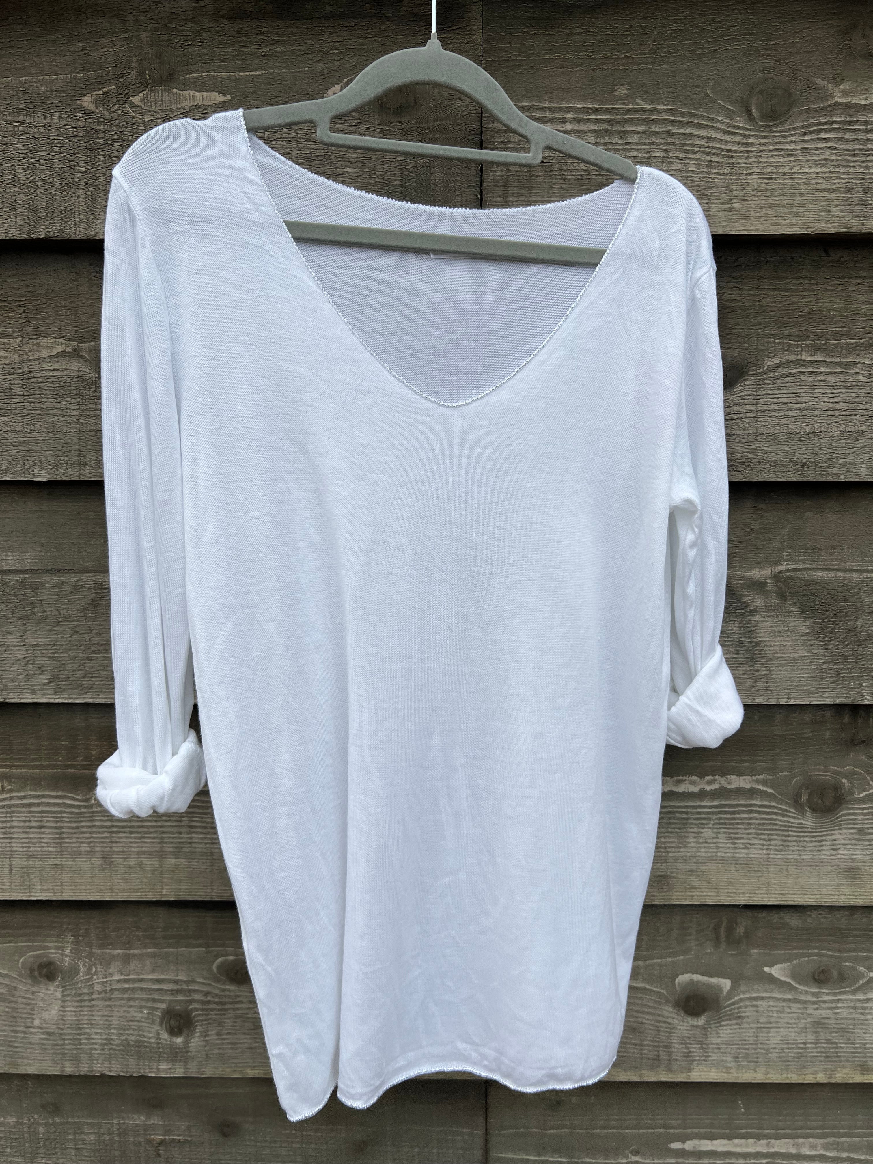 A white, long-sleeved sparkly top hanging on a wooden hanger against a wooden background.