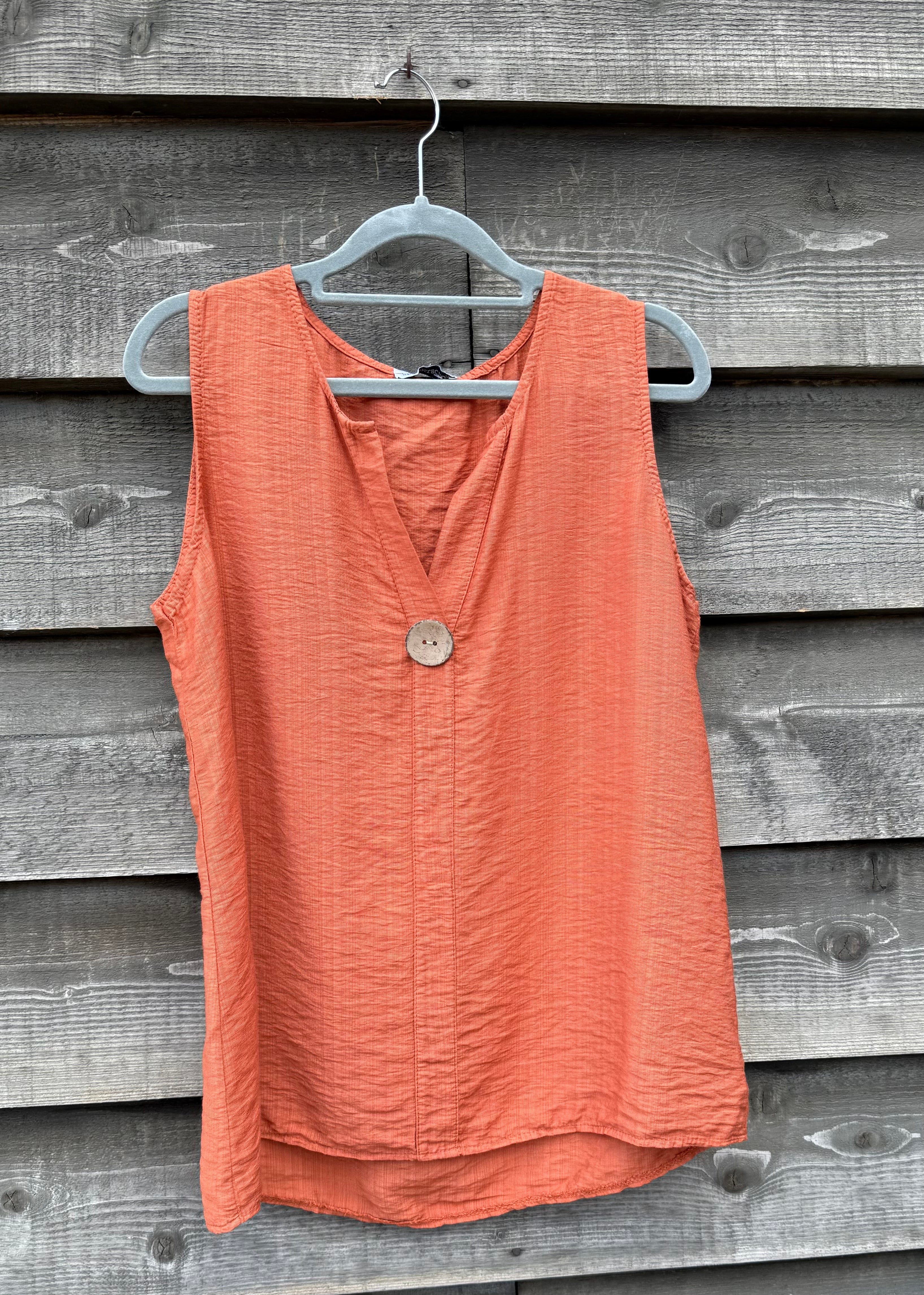 Coral sleeveless top on a hanger against a wooden background