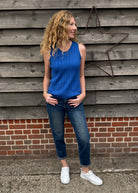 Woman wearing a blue sleeveless top and jeans standing against a wooden and brick wall.
