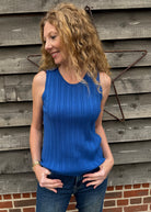 Woman wearing a blue sleeveless top standing against a wooden wall.