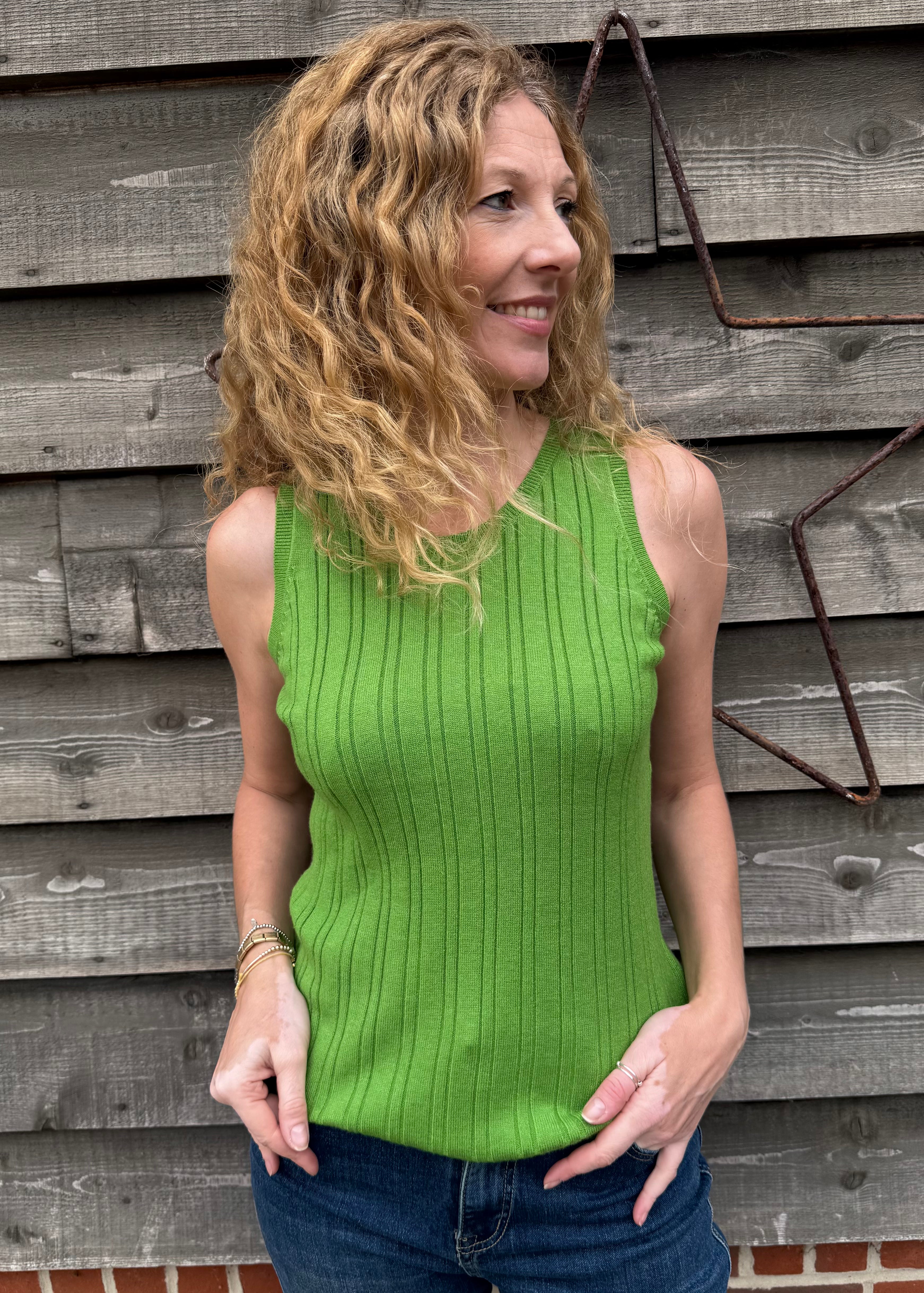 Woman wearing a green sleeveless sweater against a wooden wall.