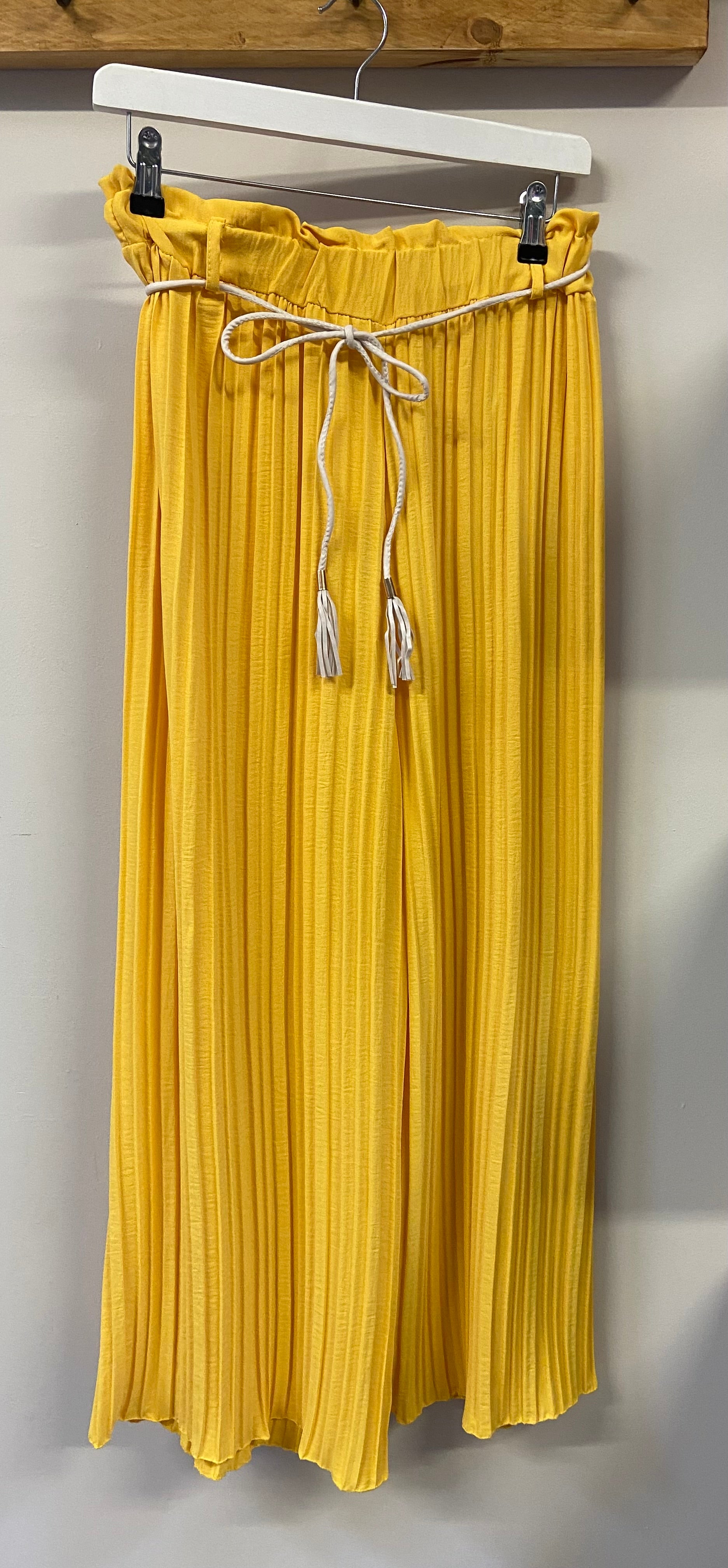 A person wearing yellow pleated trousers with a denim jacket and white shoes.