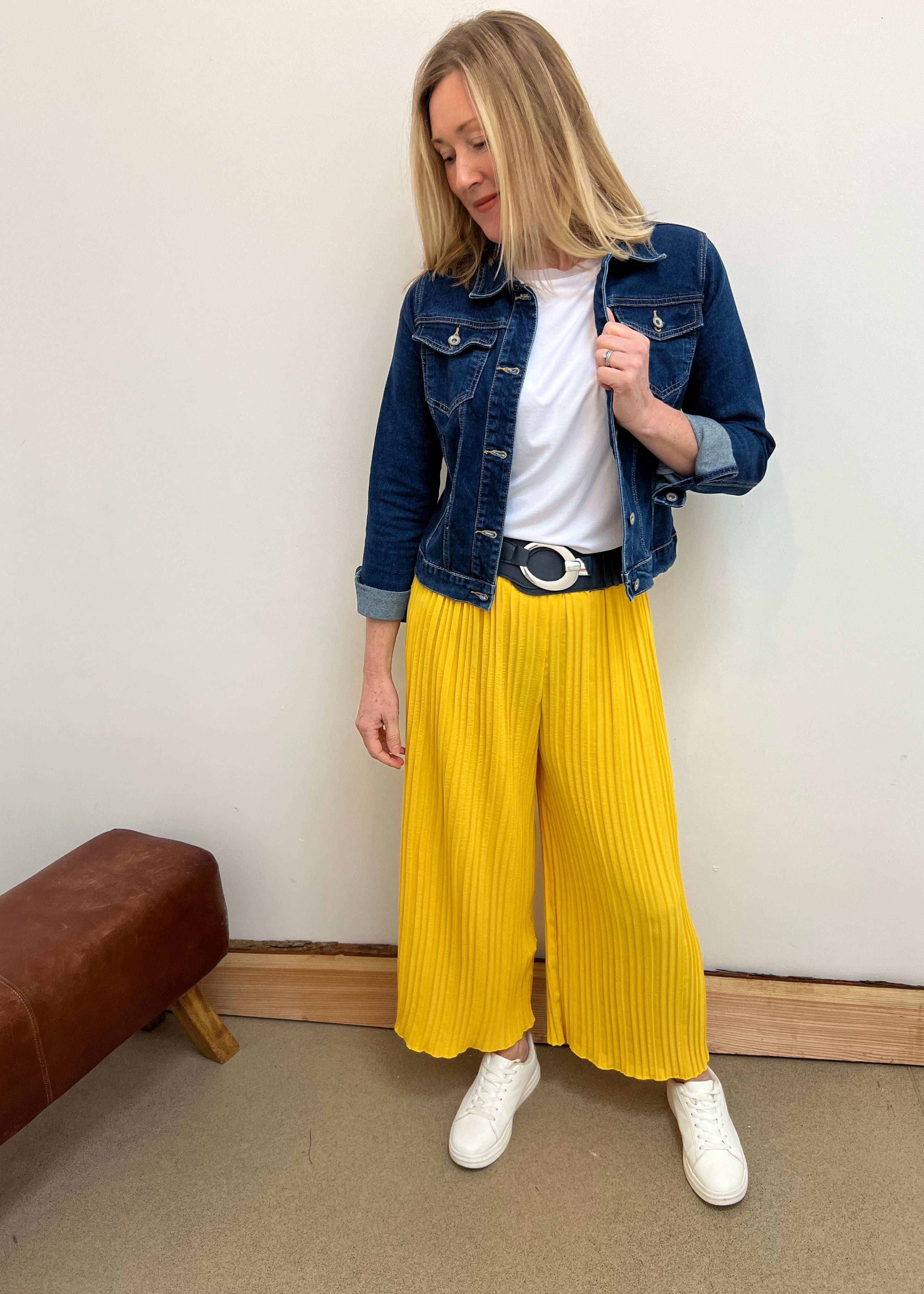 A person wearing yellow pleated trousers with a denim jacket and white shoes.