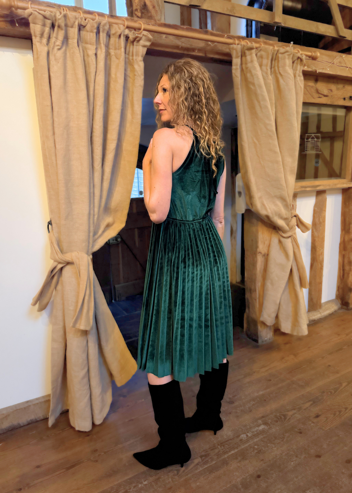 Lady wearing emerald green velvet dress showing the back of the halterneck dress style.
