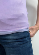 Person wearing a light purple sleeveless top and blue jeans on a plain background