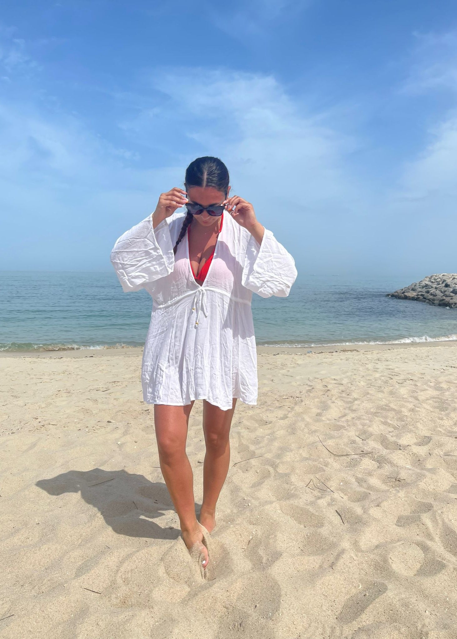A person standing on a beach wearing a white viscose kaftan dress with 3/4 length sleeves.