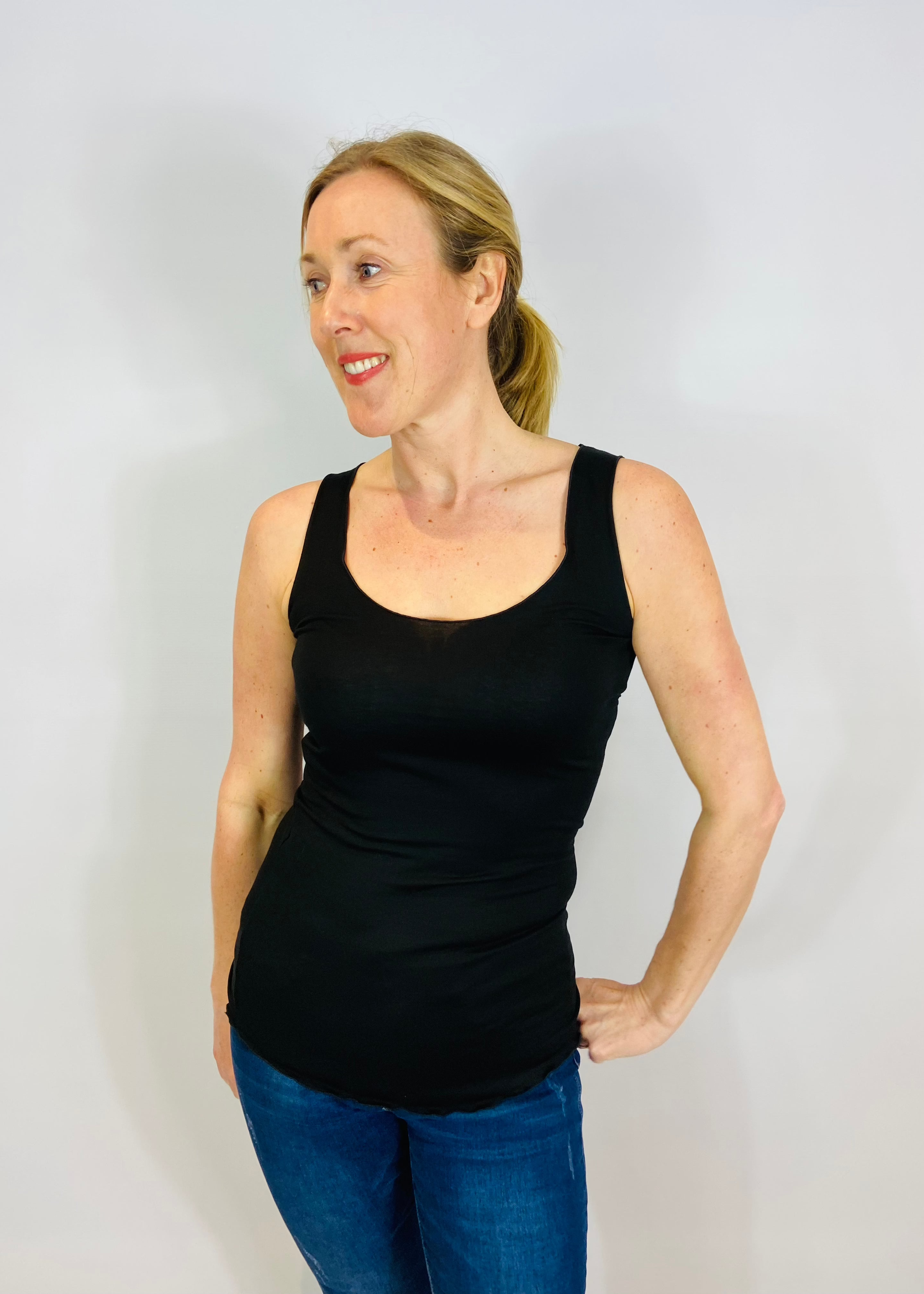 A woman wearing a black fitted tank top vest, standing against a plain background.