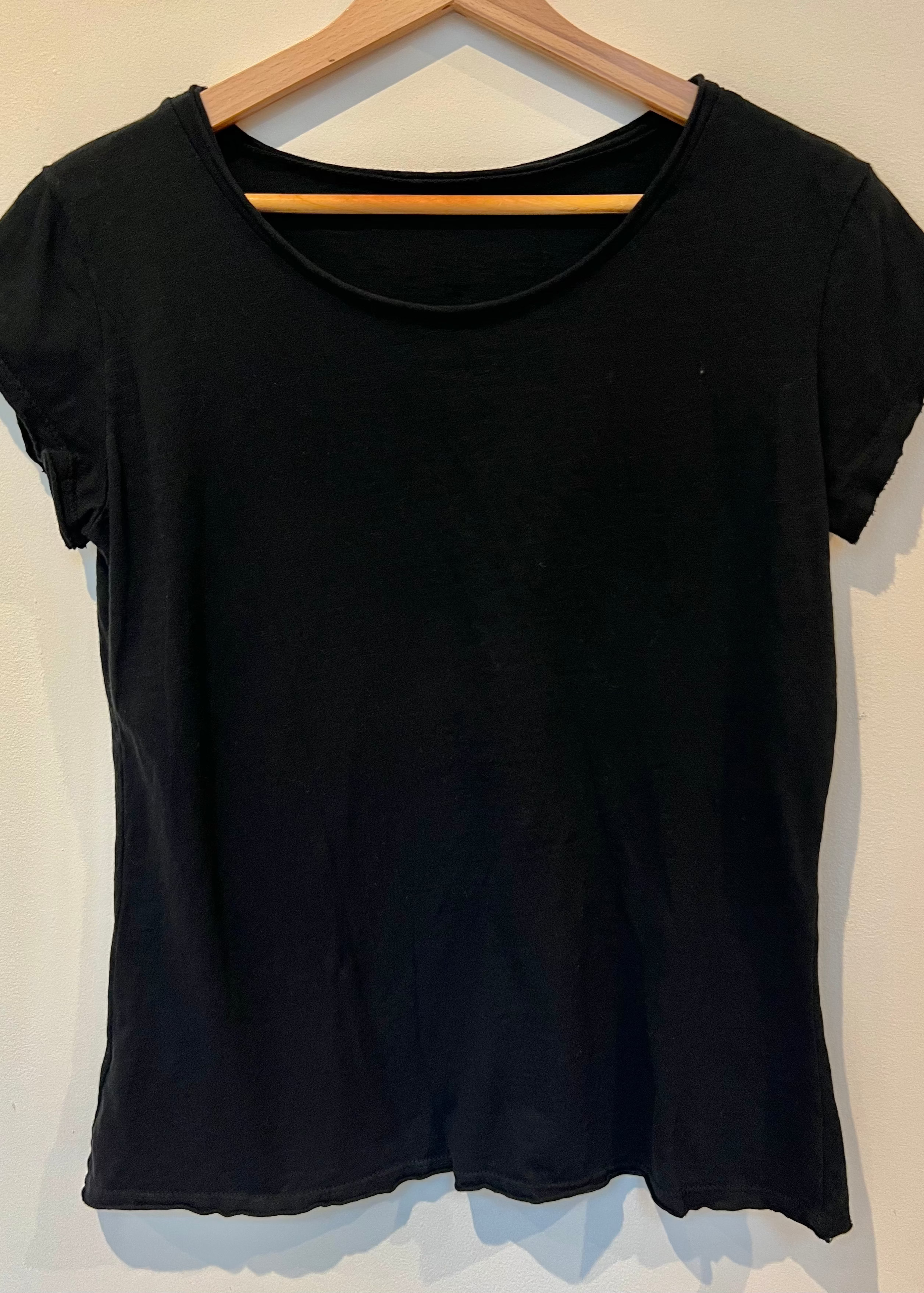 Black t-shirt on a wooden hanger against a white wall