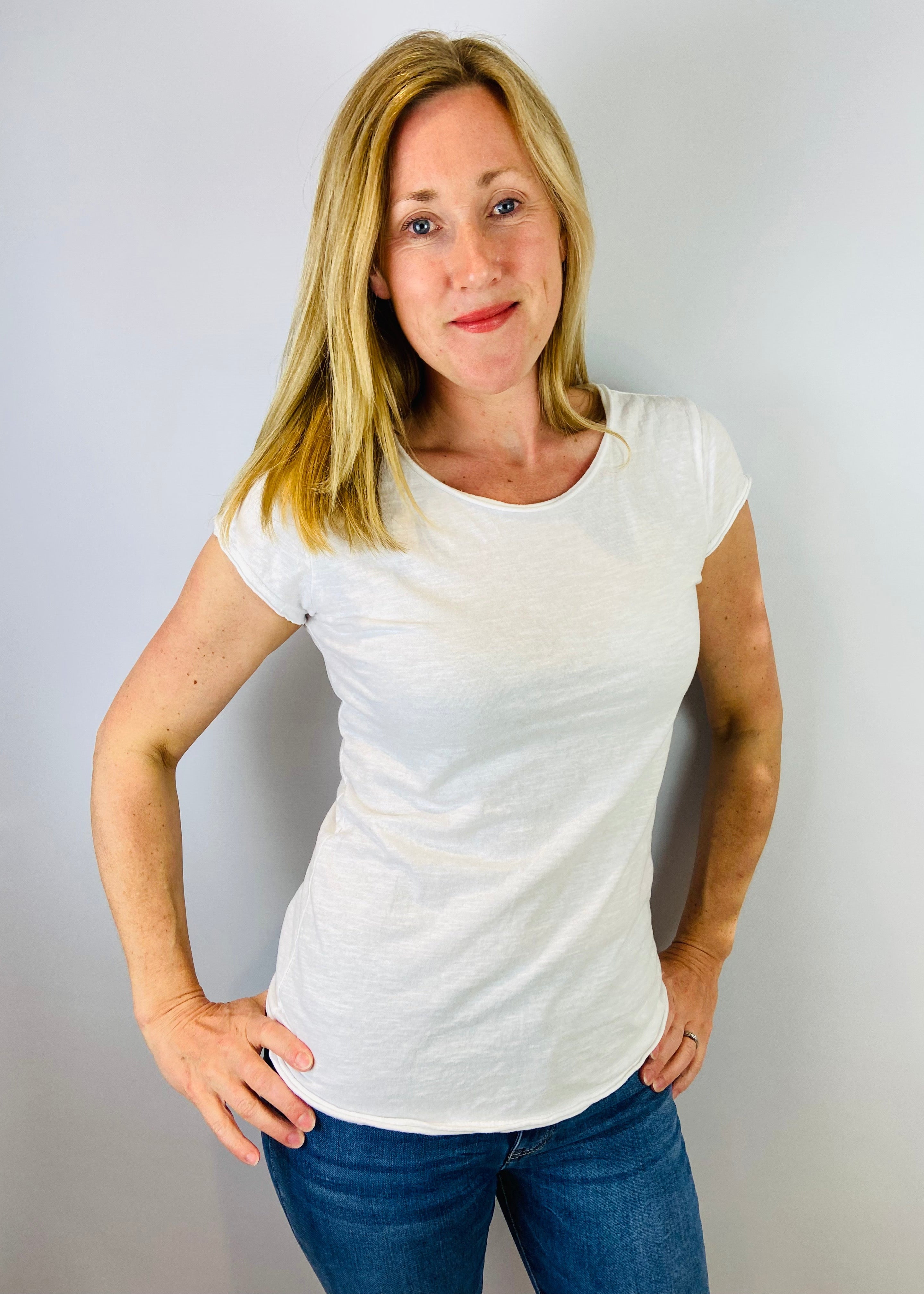 Woman wearing a white t-shirt and blue jeans against a plain background