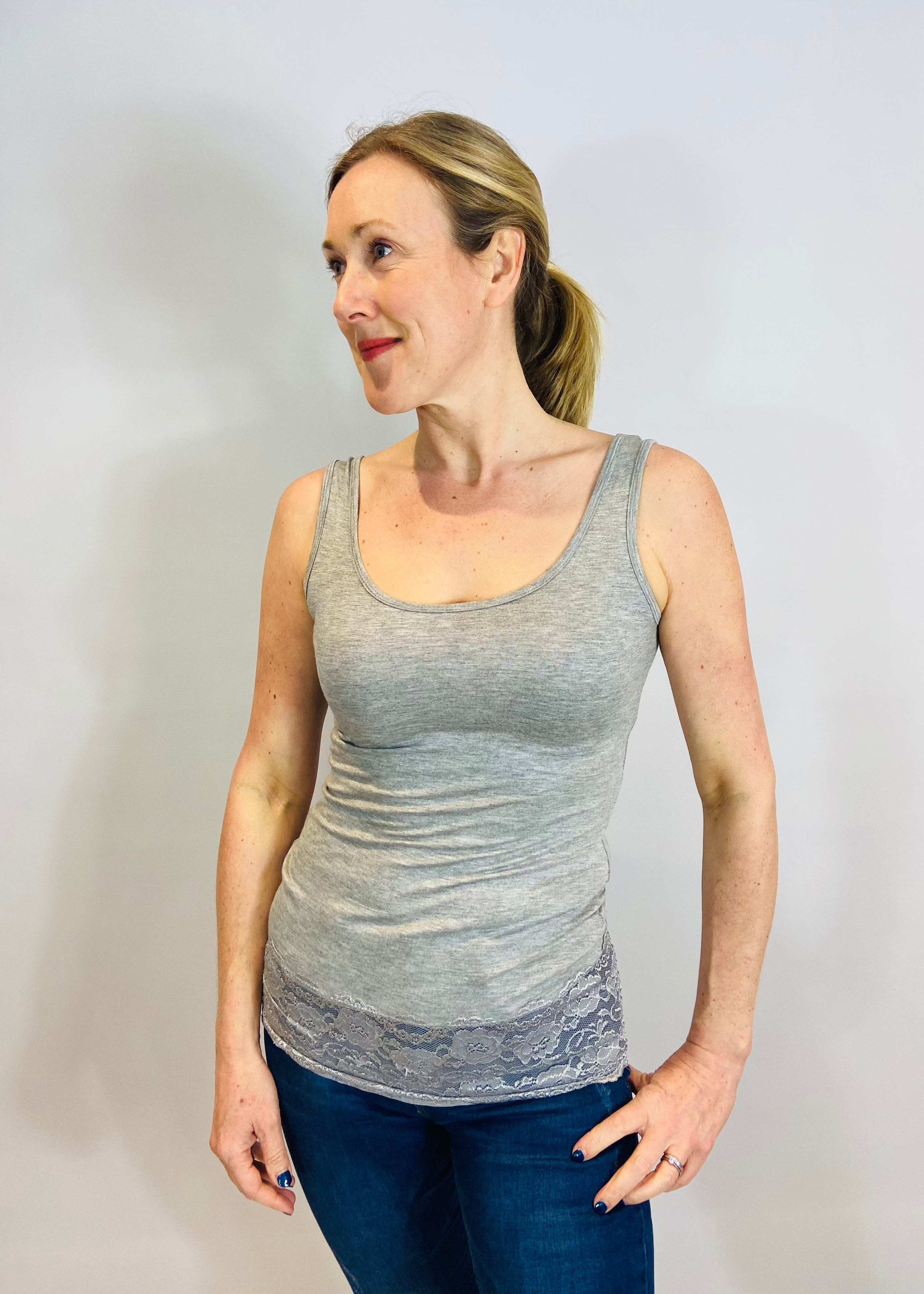 A woman wearing a gray sleeveless tank top with a laced hem, paired with blue jeans.