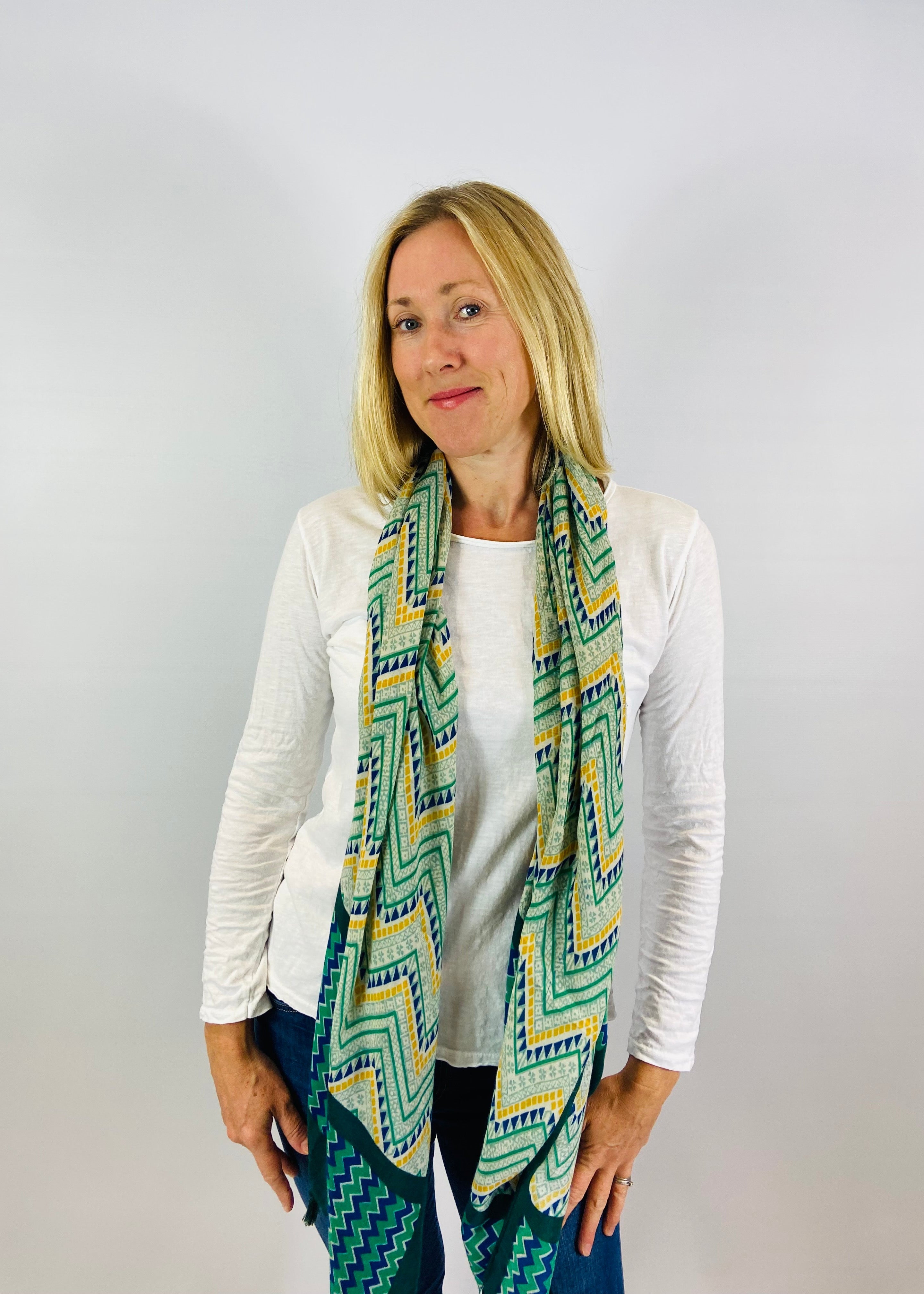 A woman wearing a white long sleeve top with a geometric patterned scarf.