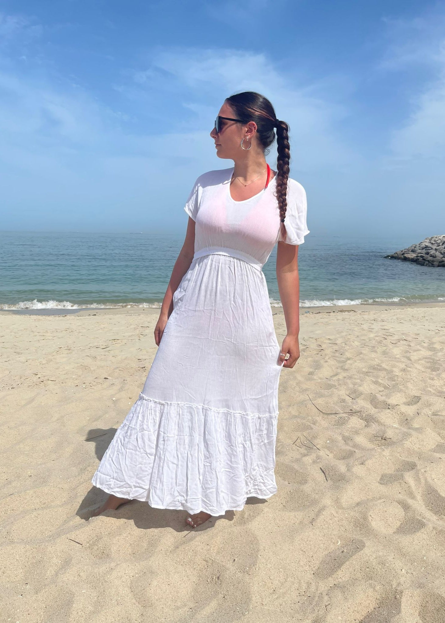 Woman in a white dress standing on a beach with ocean and sky in the background